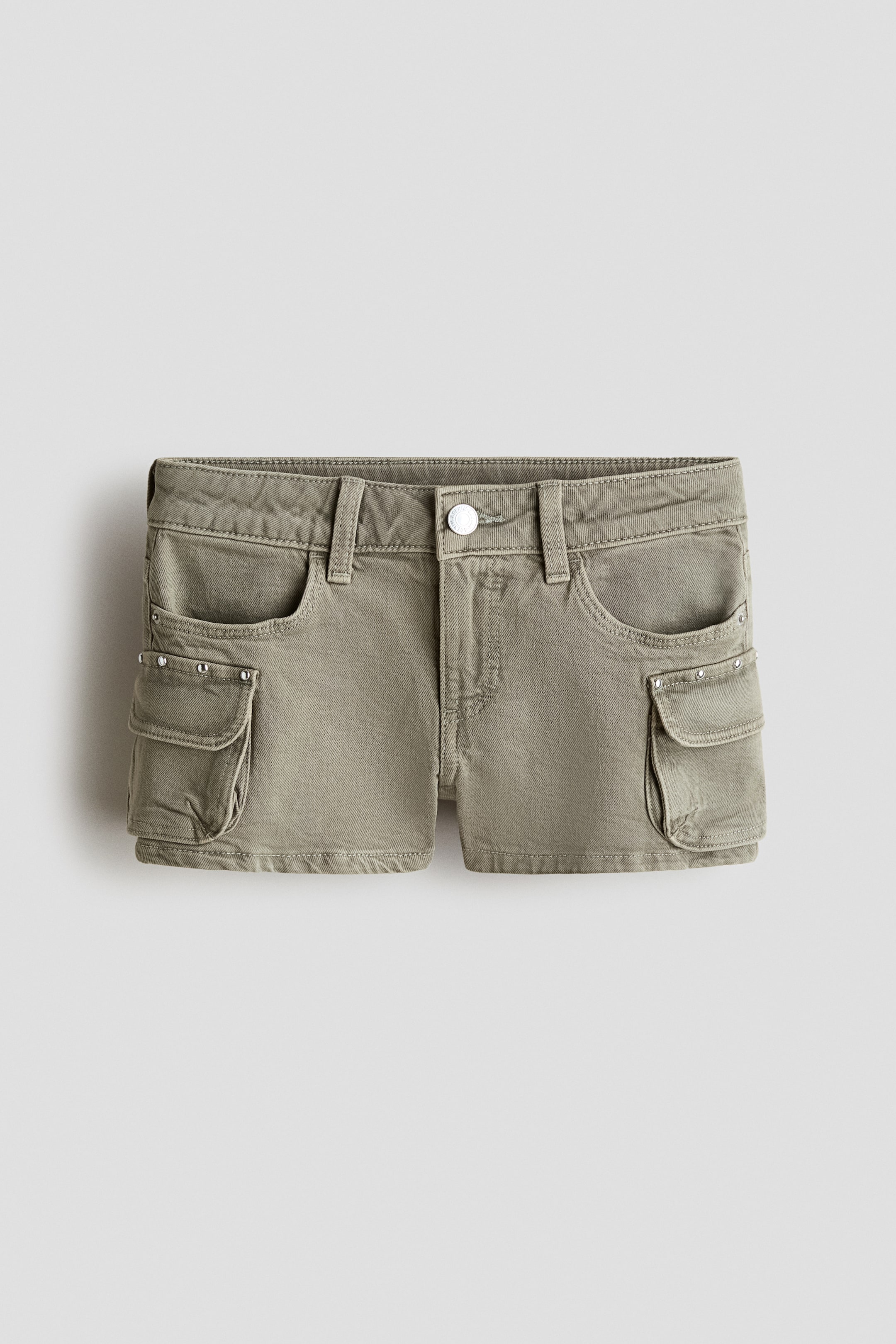 Ver imagen más grande: Los pantalones cortos cargo verde oliva se muestran en una vista frontal, con un cierre de botón en la cintura y trabillas para cinturón. Se pueden ver dos bolsillos delanteros curvados, con pequeños remaches plateados que detallan la tela debajo de sus aberturas, y dos grandes bolsillos cargo con solapa en los laterales, cada uno con dos remaches plateados en sus solapas.