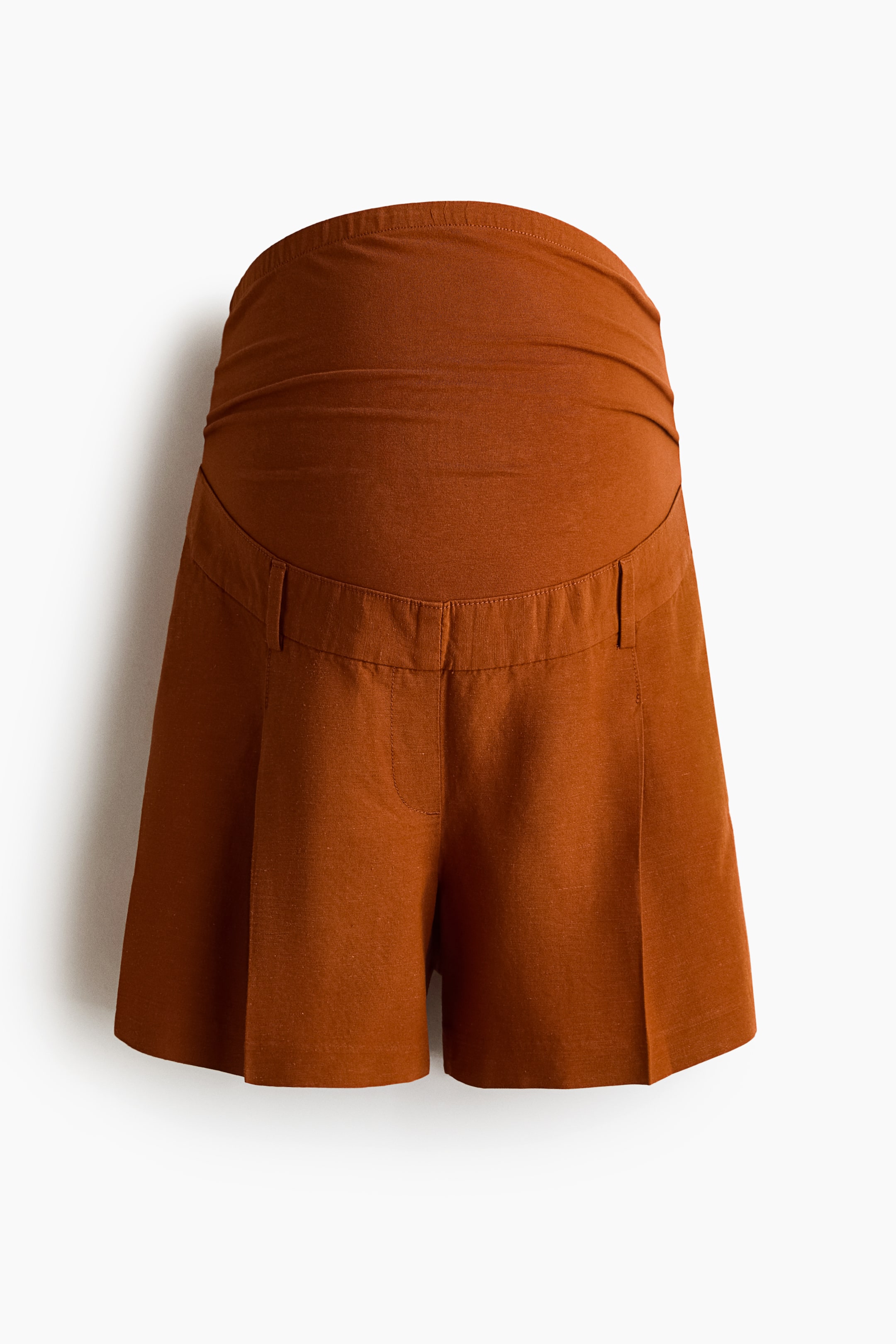 View larger image: The rust-colored tailored shorts feature a wide, ruched jersey panel at the waist for an over-the-tummy fit. The front showcases a faux fly, diagonal side pockets, pleats, and creases running down the legs.