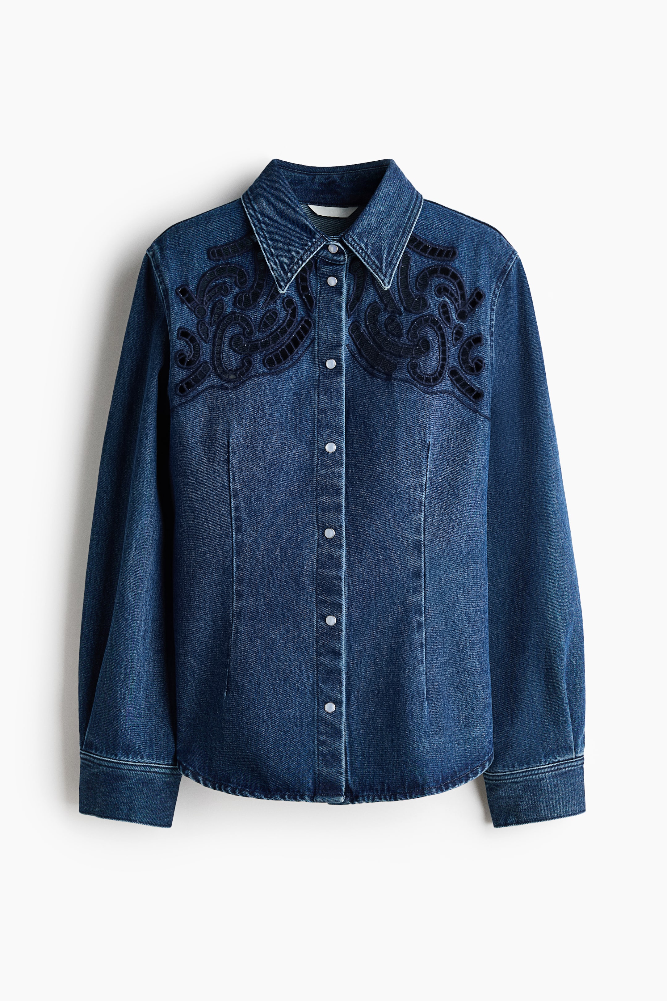 Visualizza immagine più grande: Una camicia di jeans blu scuro presenta un colletto a punta, un'abbottonatura frontale completa con bottoni a pressione di colore chiaro e maniche lunghe con polsini. Il giogo anteriore è caratterizzato da un intricato ricamo a volute blu scuro.