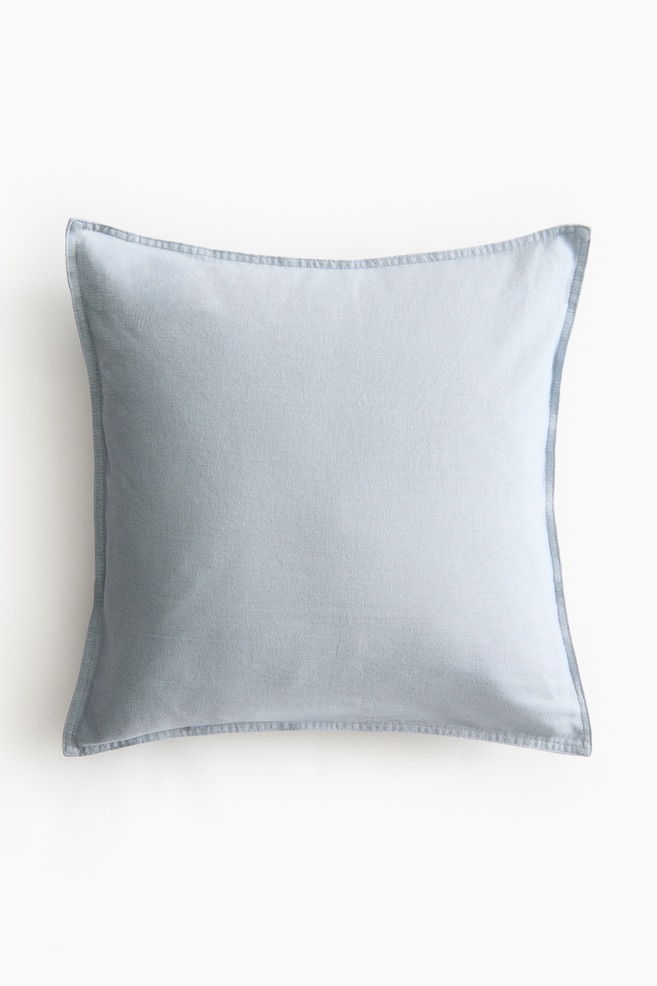 A square cushion cover is presenting its FRONT, made from a light blue linen and cotton weave. It is featuring visible stitching along all four sides, defining its edges. - 1