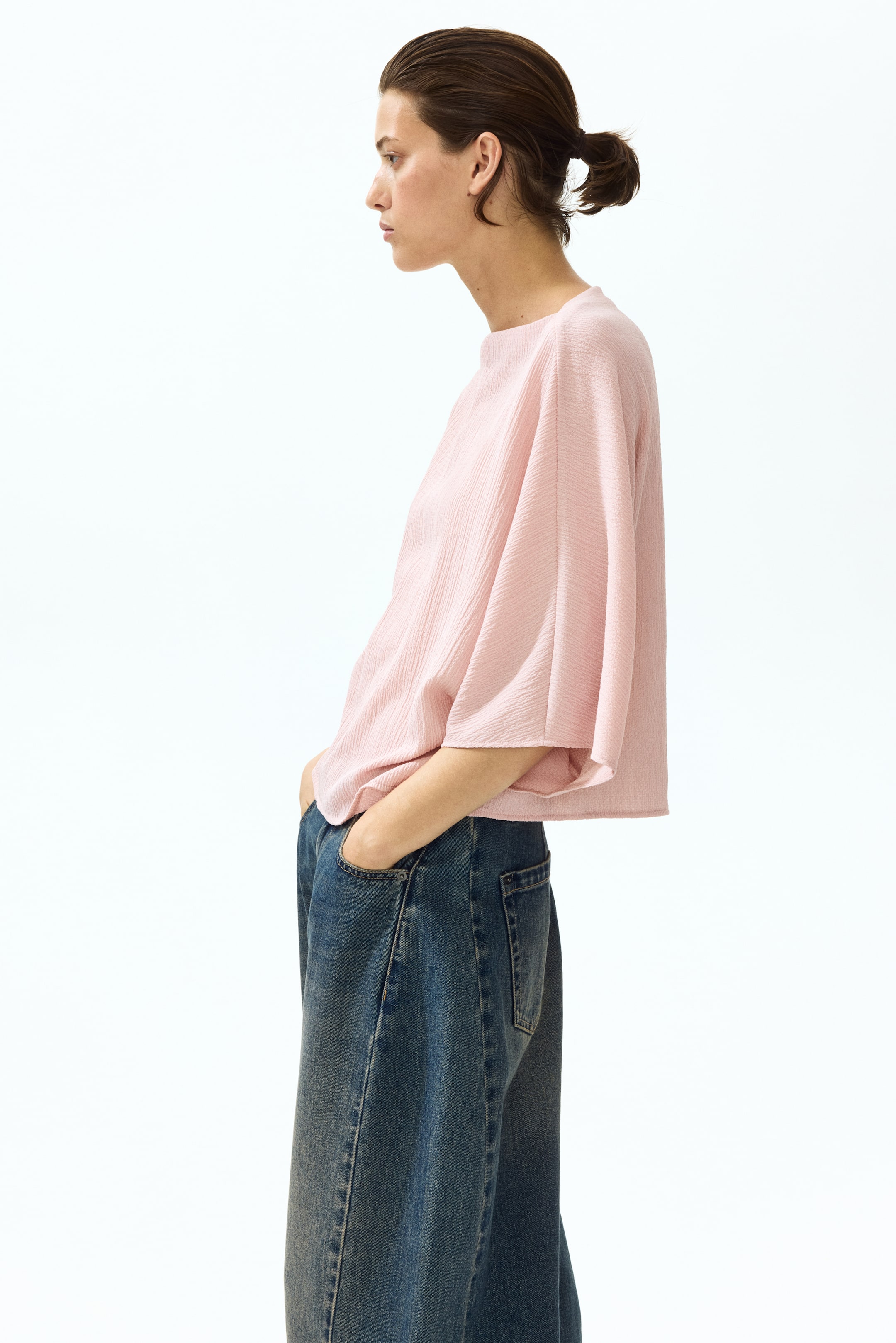 View larger image: The model is wearing a boxy-style top made from crinkled jersey, featuring a delicate boat neckline, elbow-length batwing sleeves, and a straight-cut hem.