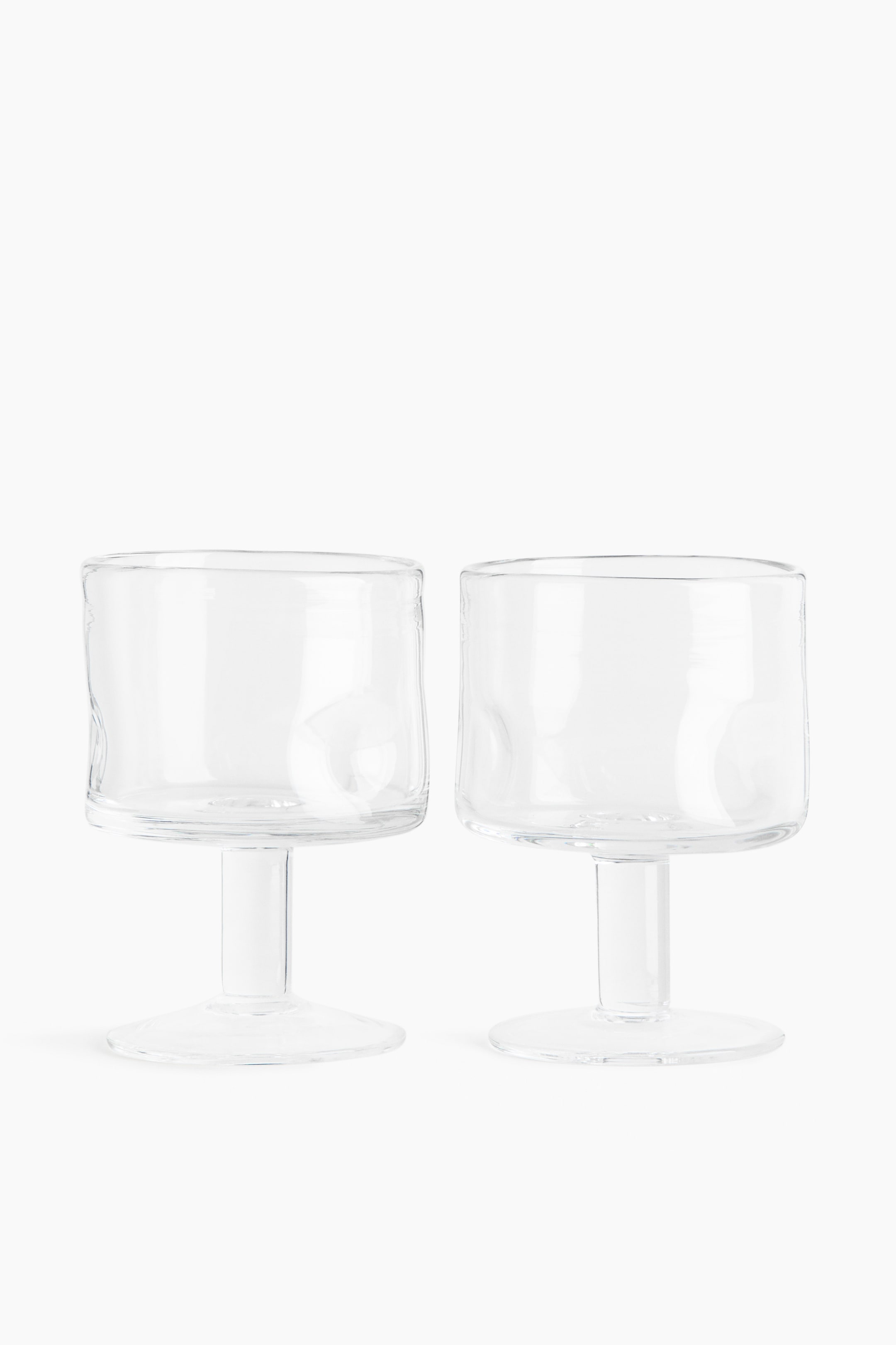 이미지 확대 보기: 두 개의 와인잔이 앞에 놓여 있으며, 두꺼운 투명 유리로 만들어진 부드럽게 둥근 모서리와 미묘하게 불규칙한 디자인을 특징으로 하는 사각형 모양을 가지고 있습니다.