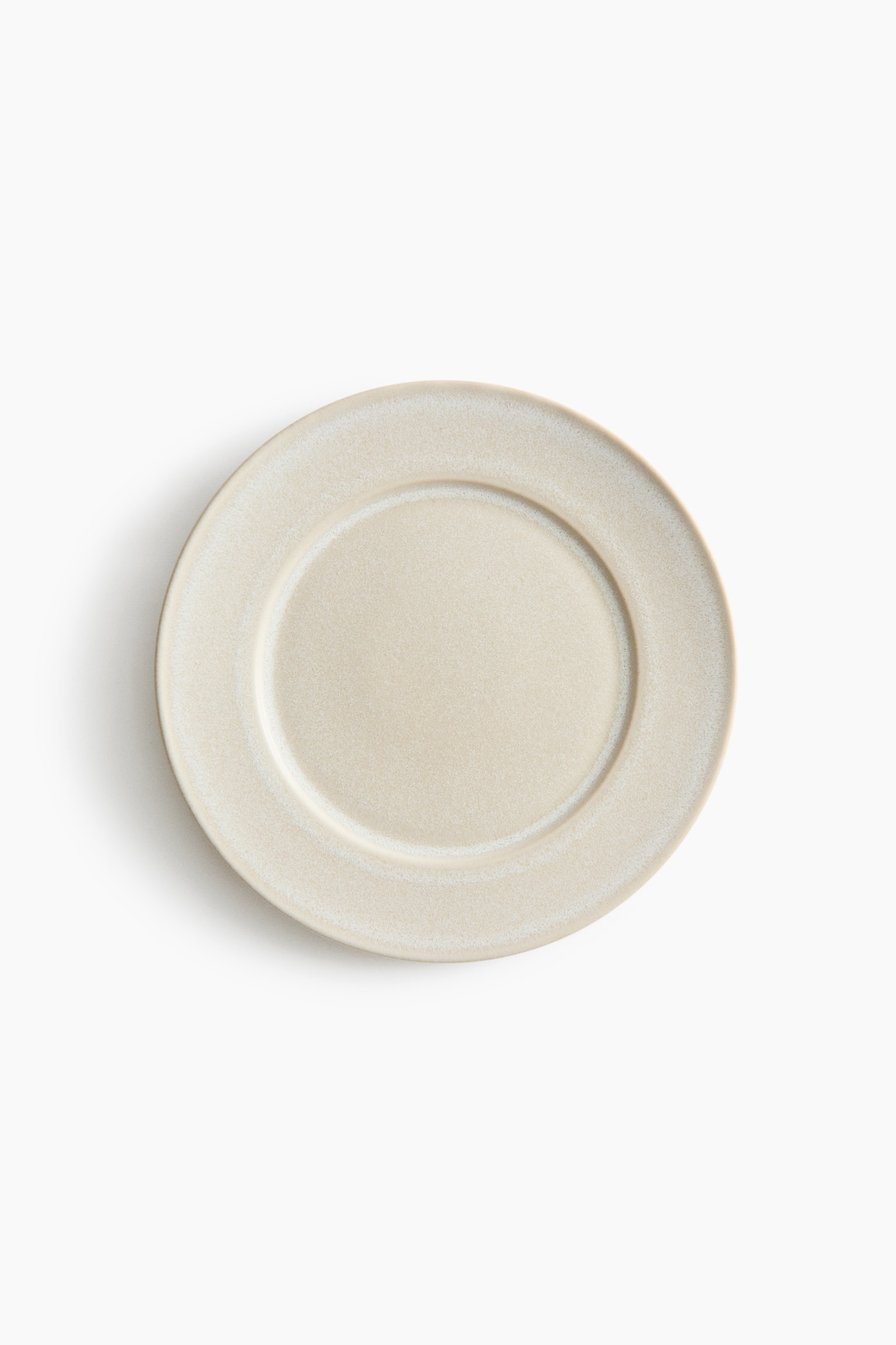 Ein runder Keramikteller liegt flach in einer Draufsicht und zeigt eine strukturierte, hellbeige gesprenkelte Glasur mit breitem Rand und einer vertieften, kreisförmigen Mitte.