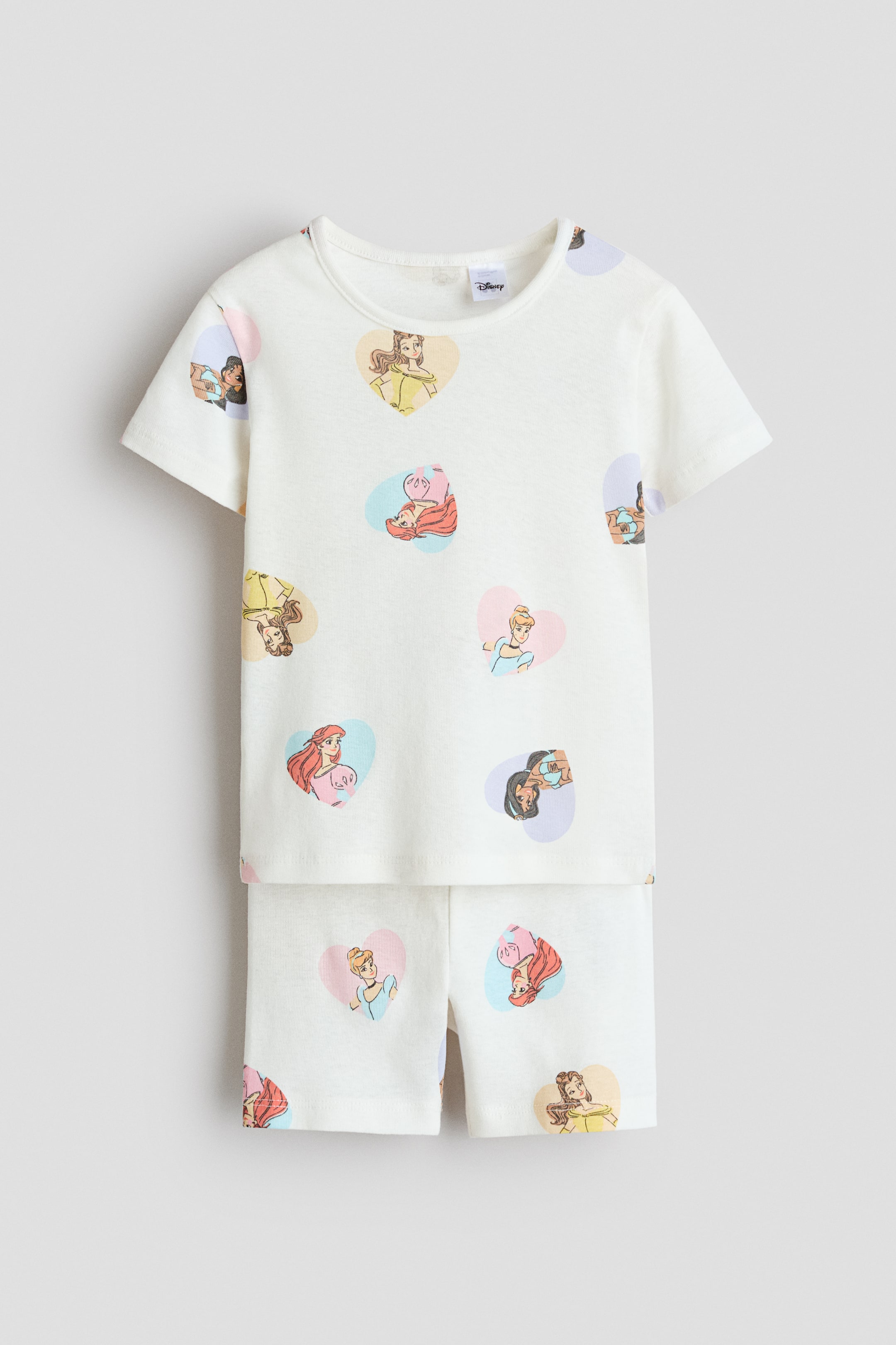 View larger image: Pajamas in printed cotton jersey are displayed front-facing, featuring a white top with a round, rib-trimmed neckline and short sleeves, along with matching shorts that have a smooth waistband. Both pieces are adorned with colorful heart-shaped motifs showcasing Disney princesses.