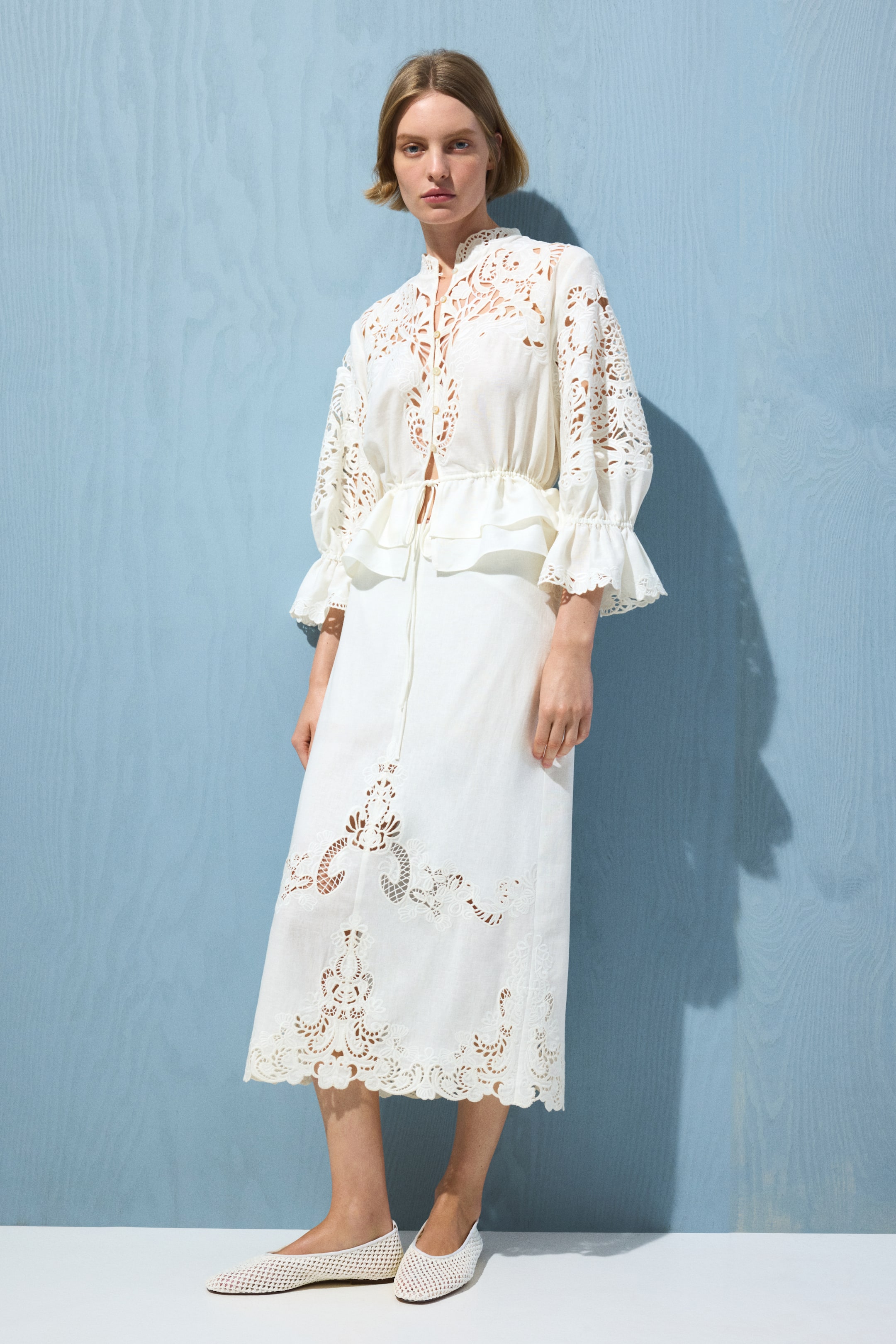 View larger image: The model is donning a calf-length skirt crafted in a breezy linen and viscose blend, accentuated with broderie anglaise panels. This high-waisted skirt showcases delicate cut-out designs, gracefully draping to mid-calf.