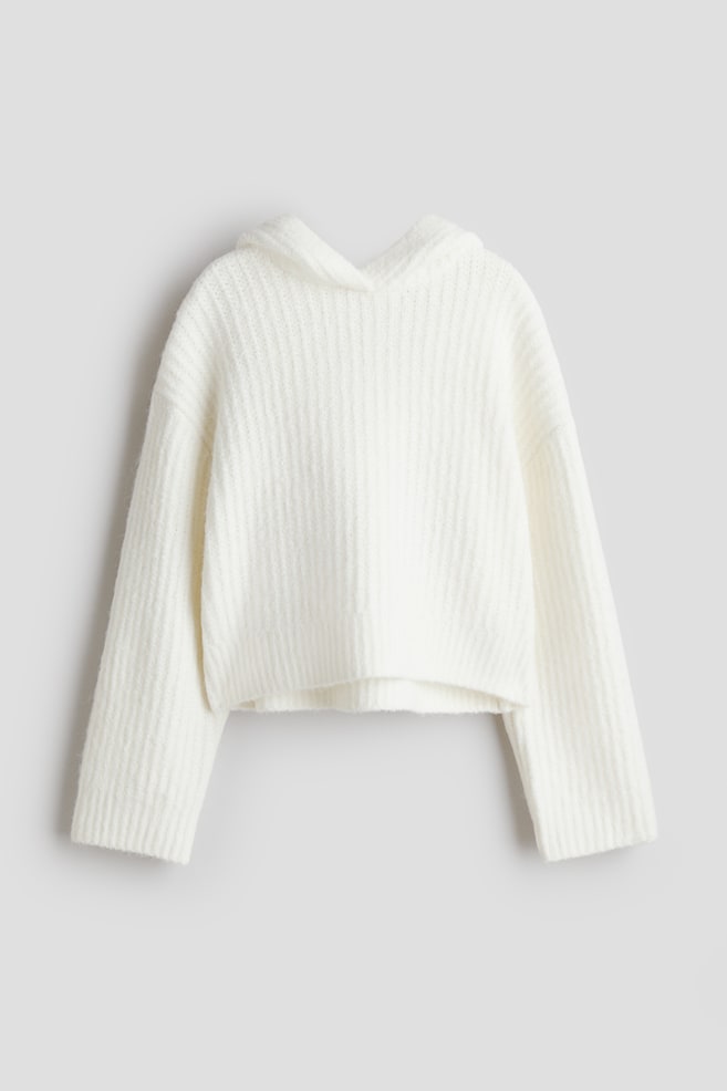 A white knitted hoodie is presenting from the front, featuring a ribbed texture throughout its relaxed, cropped silhouette. It has long sleeves with ribbed cuffs and a ribbed hem. - 1