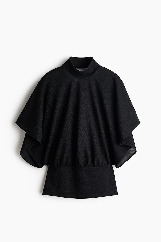 Una vista frontal muestra una blusa de punto negra que presenta cuello alto, un cuerpo holgado con caÃ­da y mangas mariposa anchas de largo hasta el codo. La tela se frunce por encima de una pretina ancha y ajustada, realzando la silueta drapeada. - 1