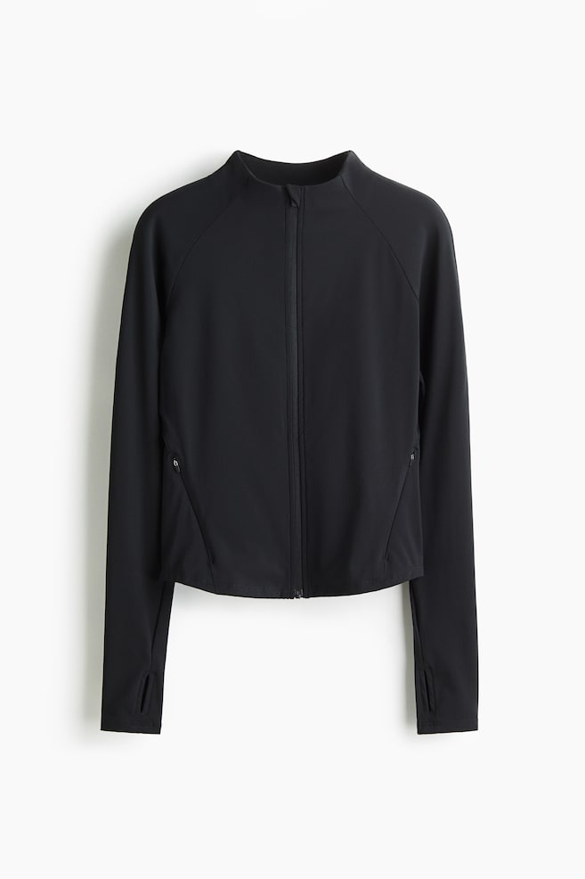 A black cropped jacket is displayed from the front, featuring a full-zip closure, a stand-up collar, and raglan sleeves. It is designed with angled zippered pockets on the lower front and thumbholes at the long sleeve cuffs. - 1