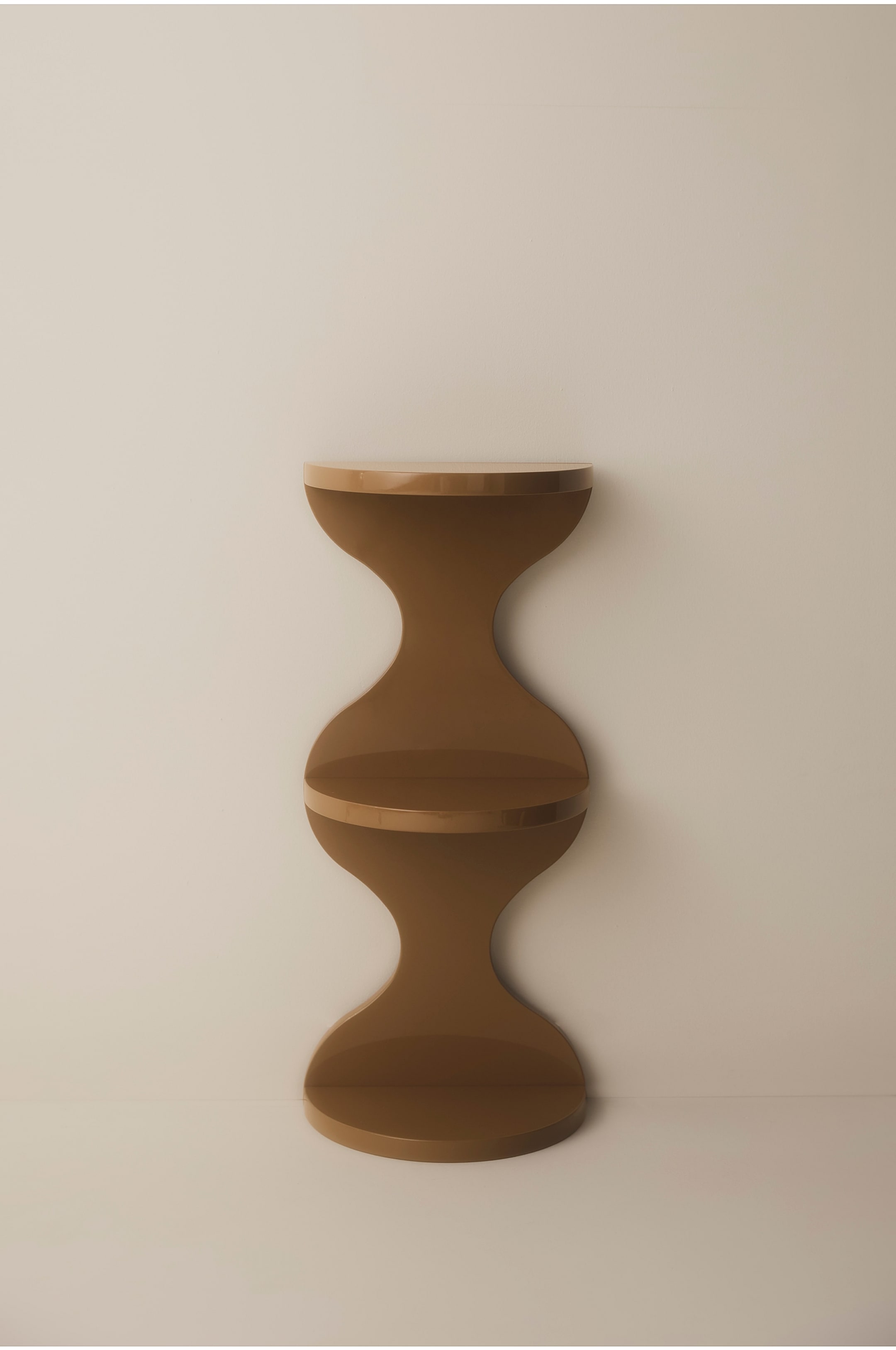 Grotere afbeelding bekijken: Een glanzend, karamelbruin rek staat frontaal opgesteld en toont een sculpturale, golvende silhouet met drie halfronde legplanken. Het stuk heeft een gladde, reflecterende afwerking met een gebogen, zandloperachtige verticale steun.