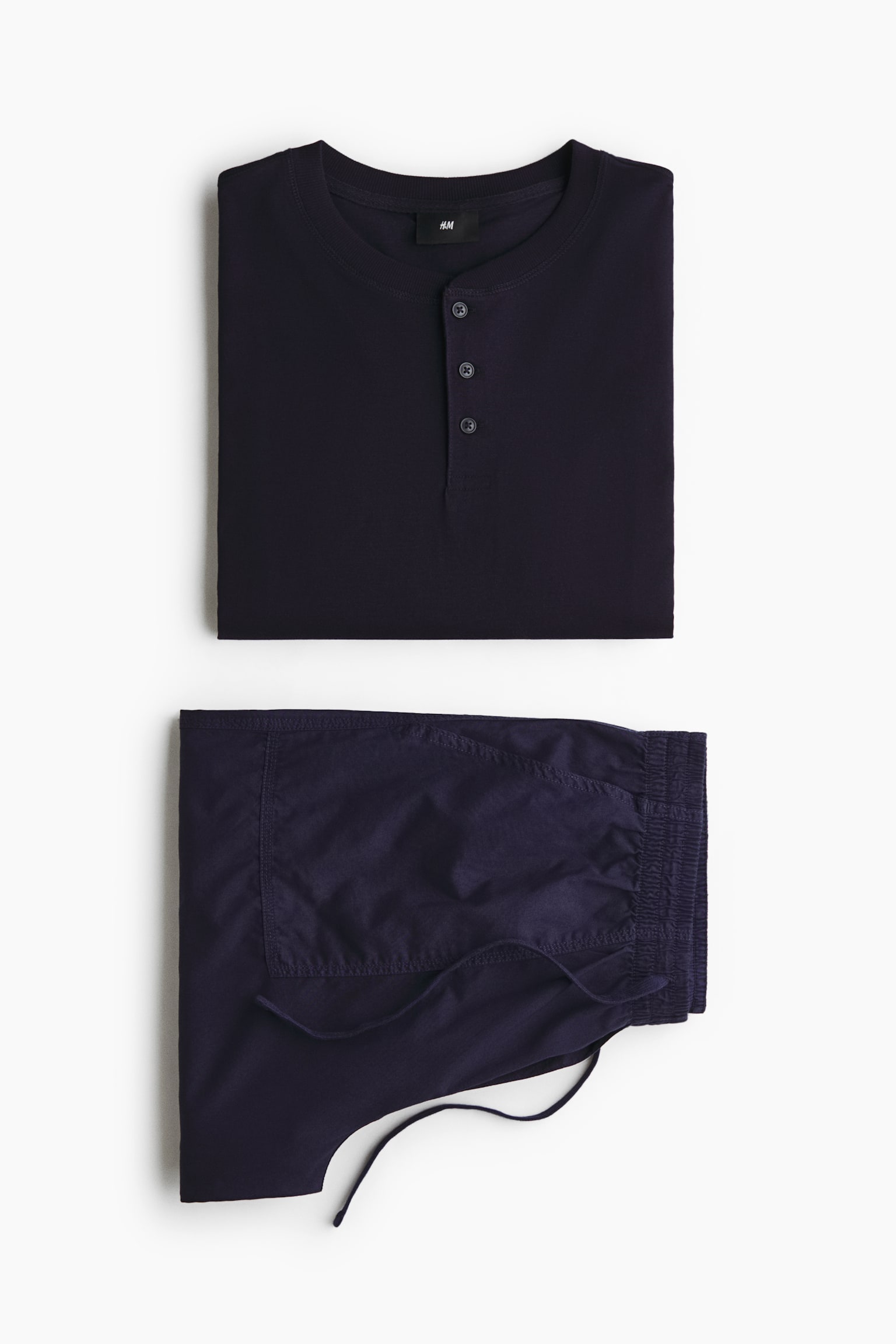 A folded dark navy loungewear set is shown from the front, featuring a henley shirt and matching trousers. The top has a round neck with a three-button placket, and the folded trousers display an elastic drawstring waistband.