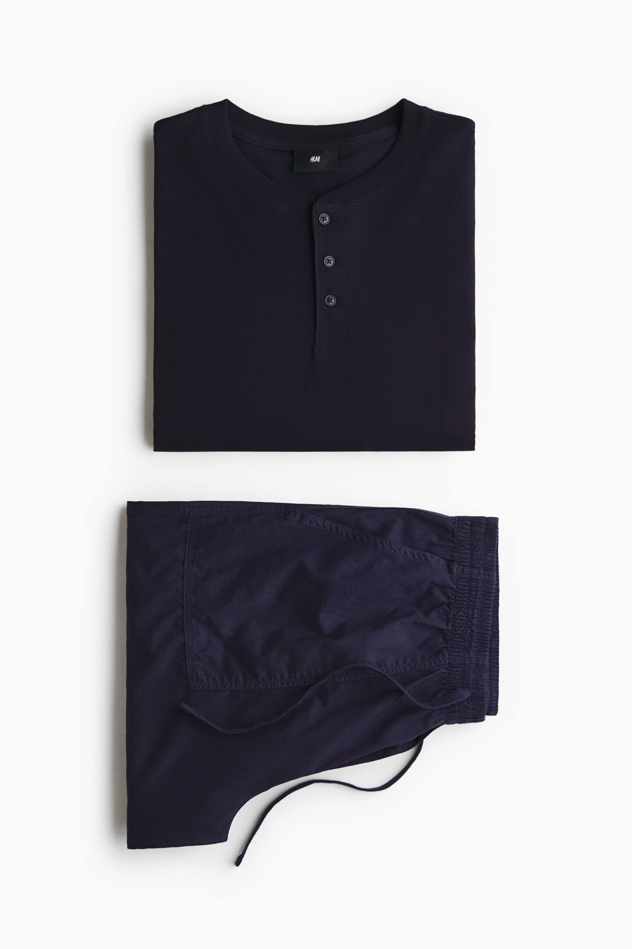 View larger image: A folded dark navy loungewear set is shown in a front view, featuring a henley shirt and matching trousers. The top has a round neck with a three-button placket, and the folded trousers display an elastic drawstring waistband.