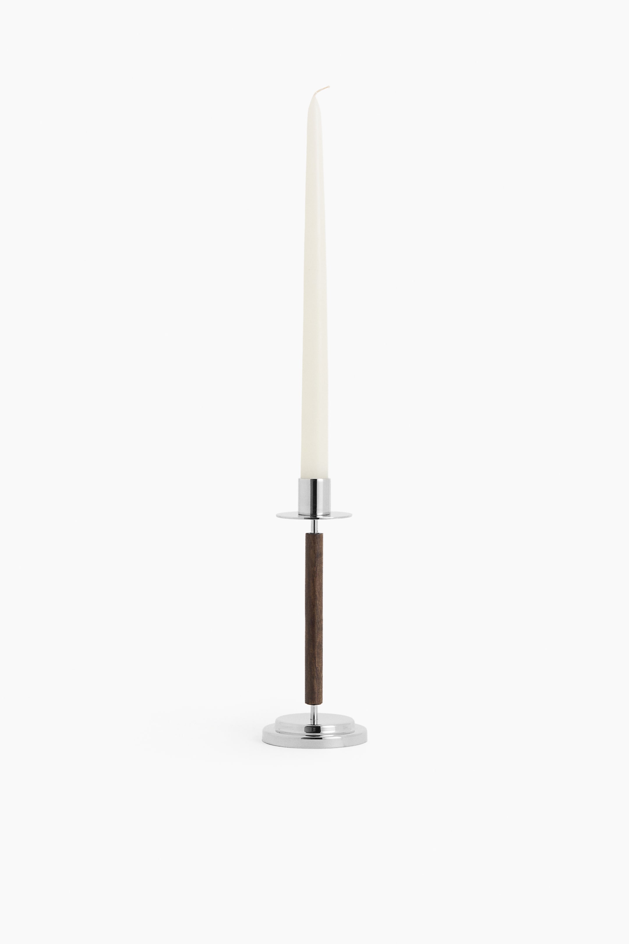 View larger image: A candlestick is standing upright, featuring a round, polished chrome base and a dark wooden shaft. A tall, slender white candle is fitted into a chrome holder at the top.