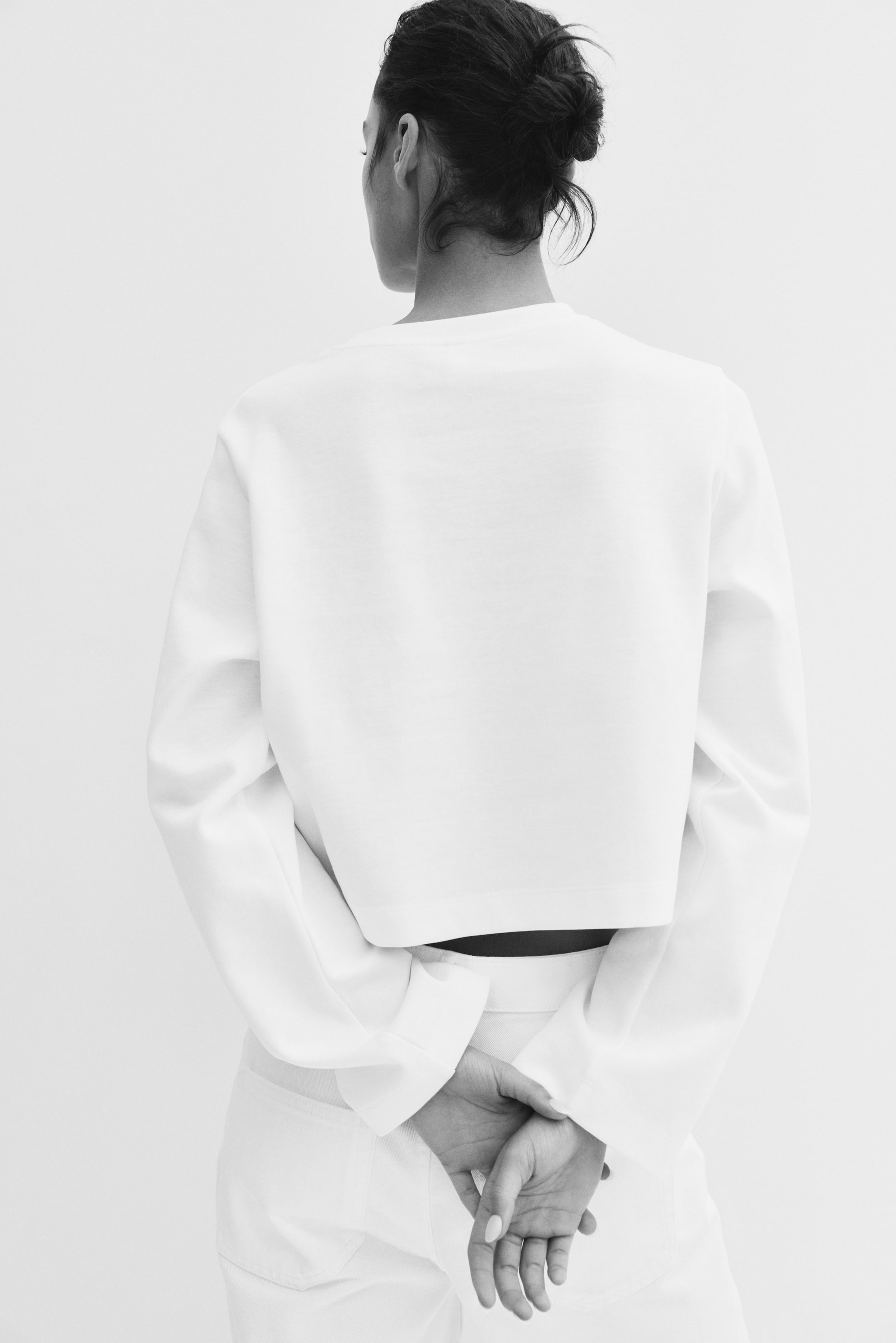 View larger image: The model is standing with their hands clasped behind their back, below the top's hem.