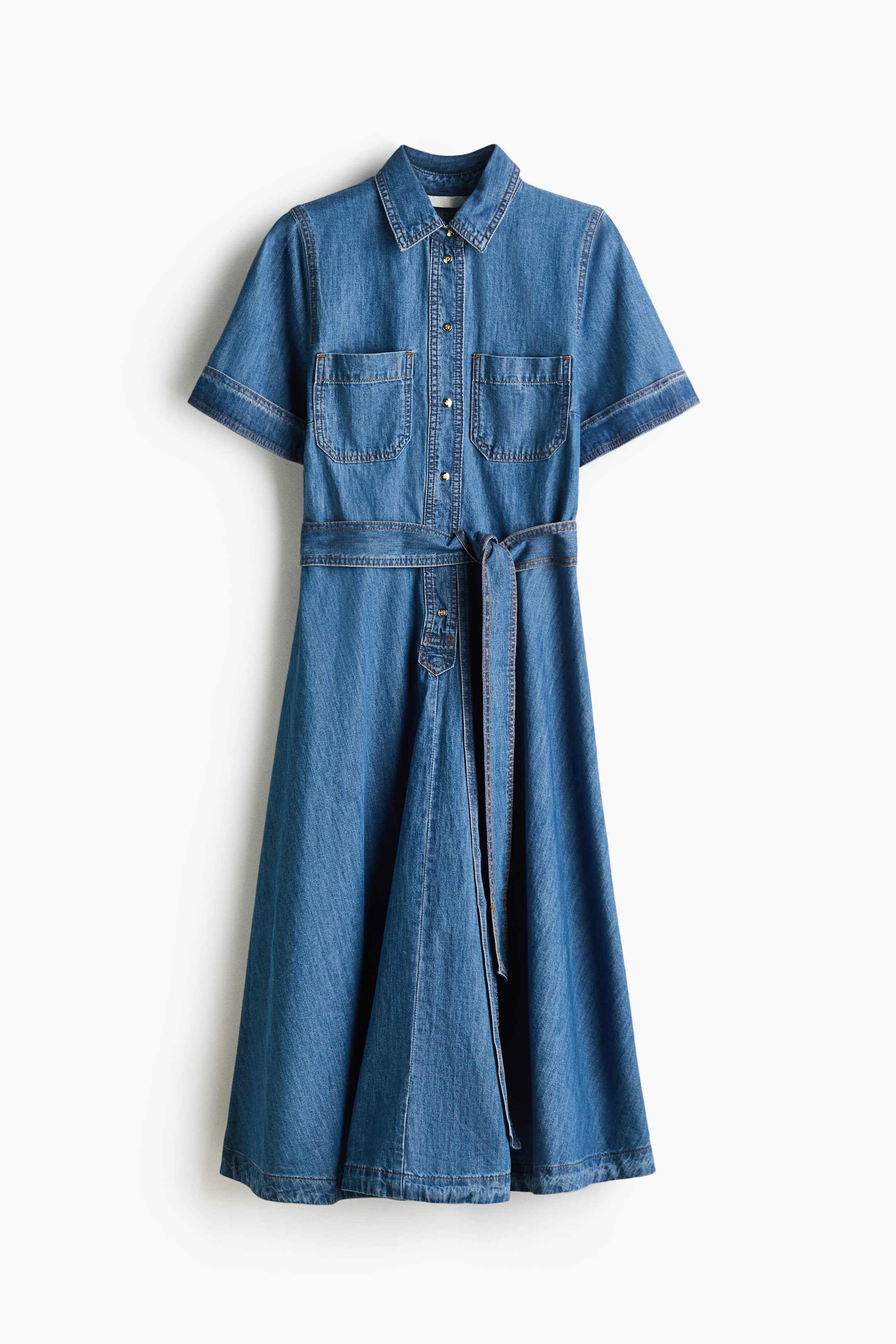 View larger image: A calf-length dress in cotton denim is shown from the front, featuring a collar, motif-detail press-studs along the front, and short sleeves with turn-up cuffs. Patch chest pockets are visible, a tie belt cinches the waist, and a flared skirt completes the design.