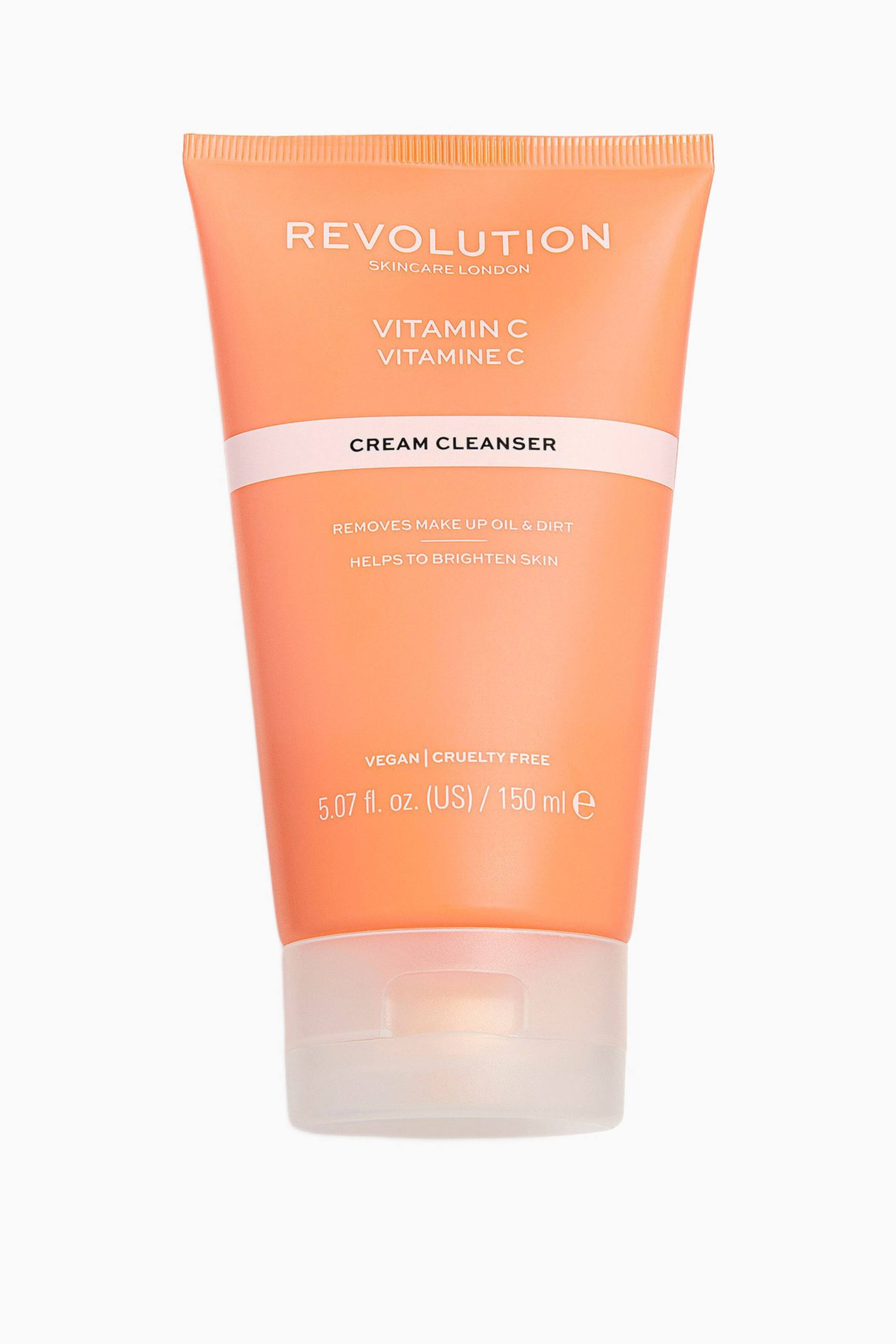 Größeres Bild ansehen: Eine pfirsichfarbene Squeeze-Tube des Revolution Skincare Vitamin C Cream Cleanser steht aufrecht und zeigt nach vorne. Auf der Vorderseite sind aufgedruckte Produktinformationen zu sehen, darunter ein hellrosa horizontaler Streifen, und die Tube steht auf einer halbtransparenten Klappkappe.