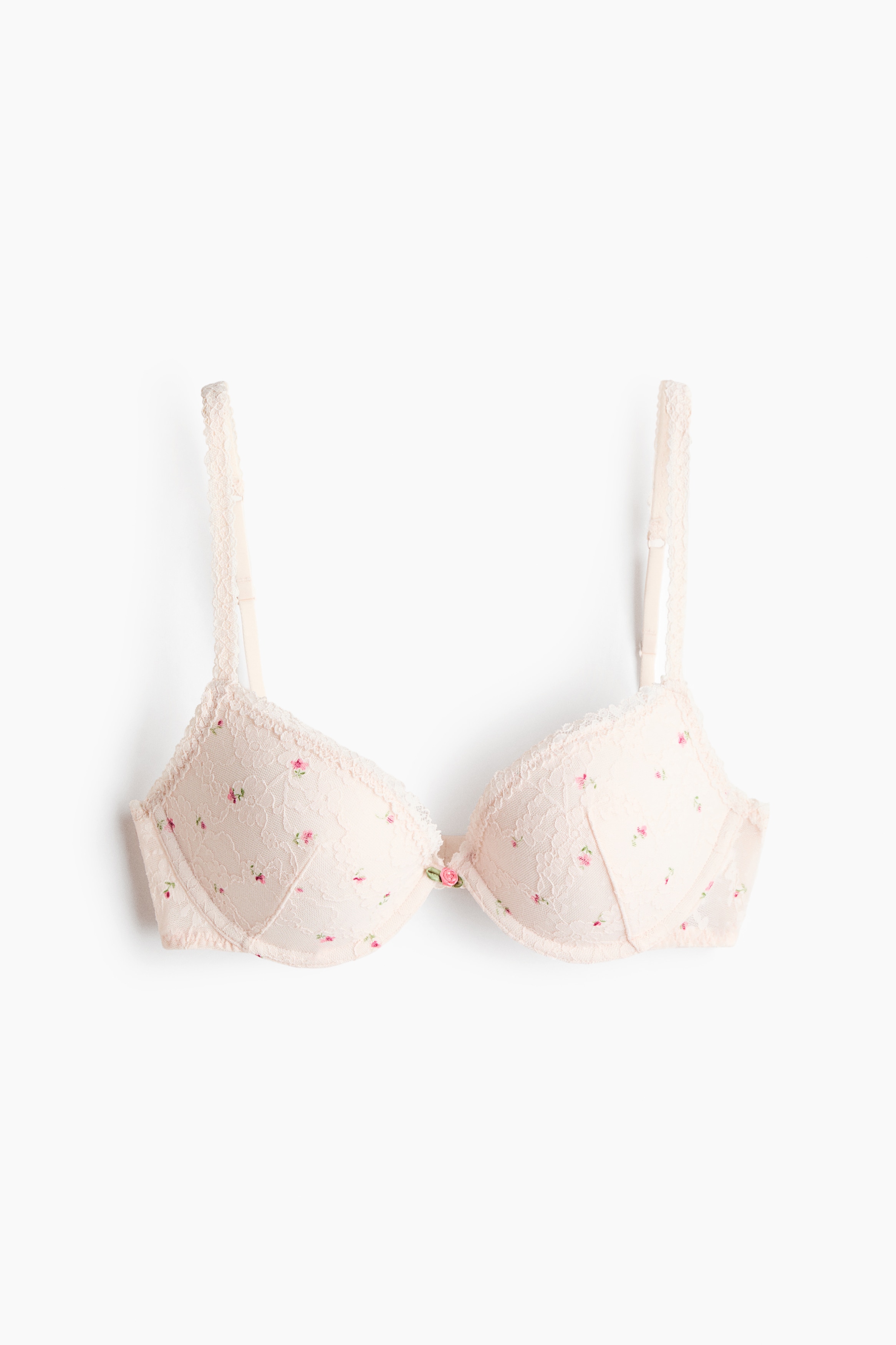La modelo lleva puesto un sujetador push-up de encaje blanco con un pequeÃ±o estampado floral rosa y un diminuto detalle de rosa en el centro. El sujetador presenta copas con aro y ribetes de encaje festoneado a lo largo de los bordes y los tirantes.