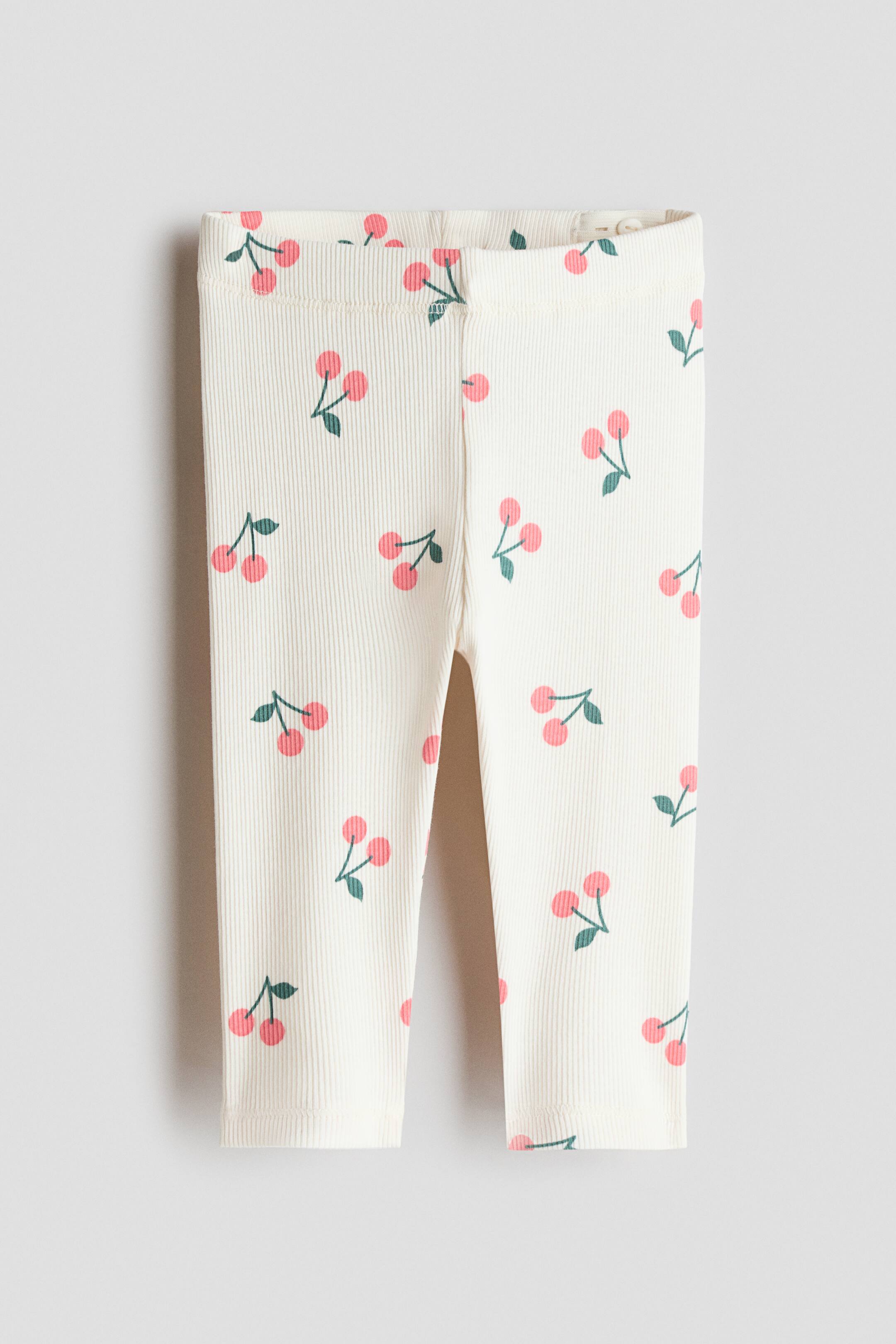 View larger image: Cream ribbed leggings feature a recurring cherry motif with pink fruit and green stems. An elasticated waistband is evident at the top.