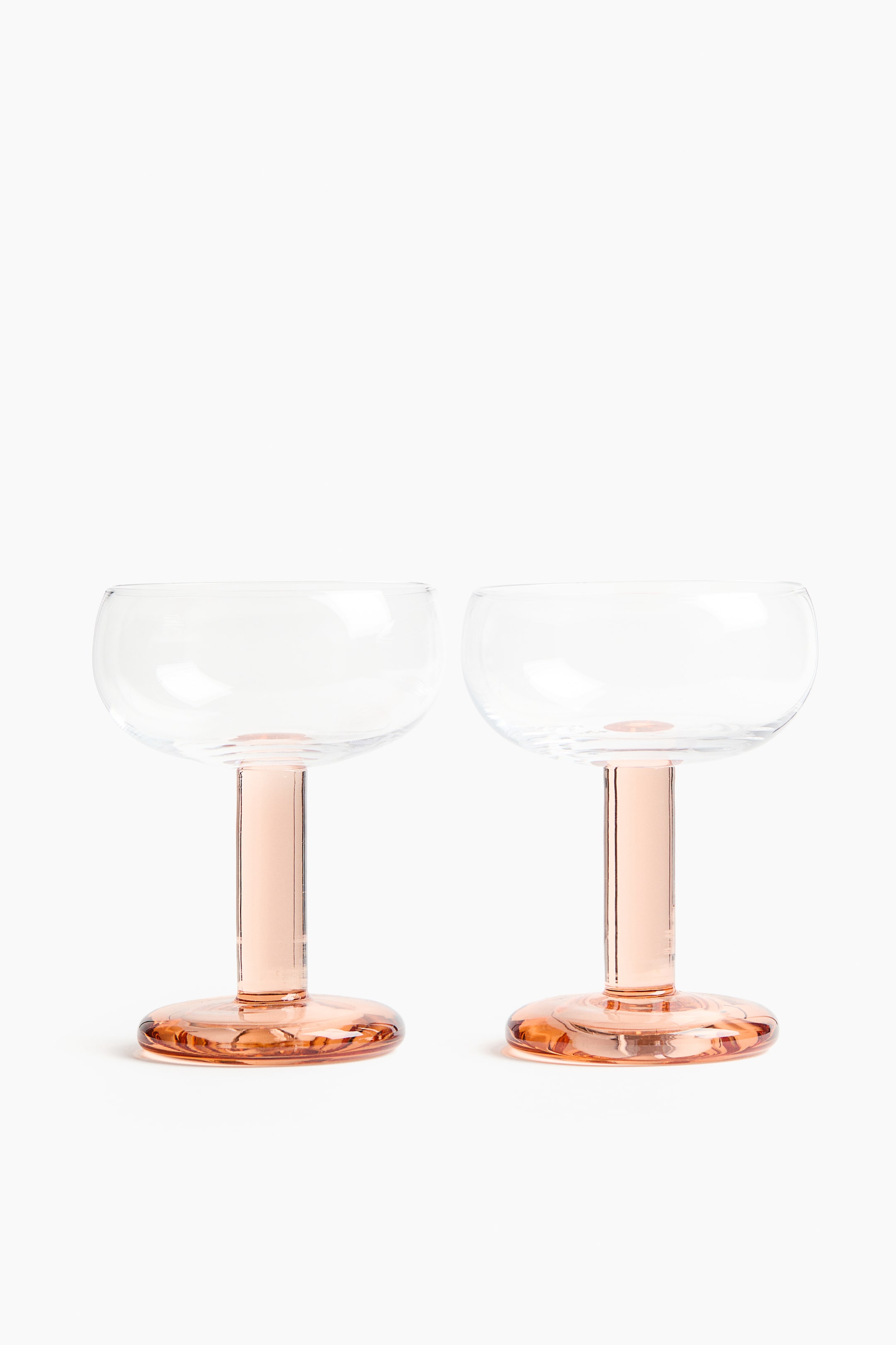 View larger image: Two hand-blown glass coupes are shown FRONT facing, each featuring a softly rounded clear bowl, a bold tinted stem, and a matching tinted base.