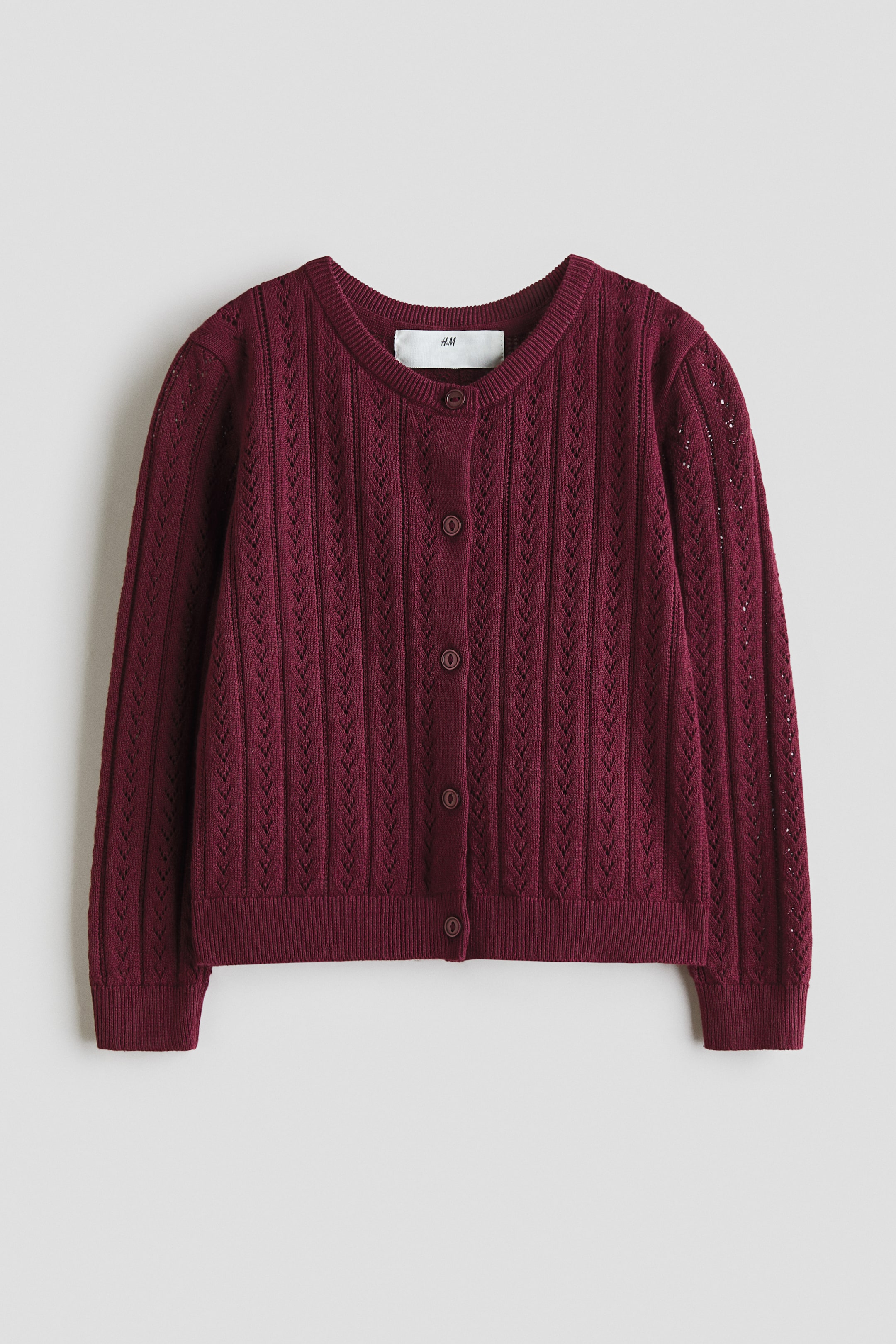 Agrandir l'image: Un cardigan bordeaux en maille pointelle douce en coton, avec un col rond à bord-côtes. Il est également conçu avec cinq boutons sur le devant, et des finitions côtelées aux poignets et à l'ourlet.
