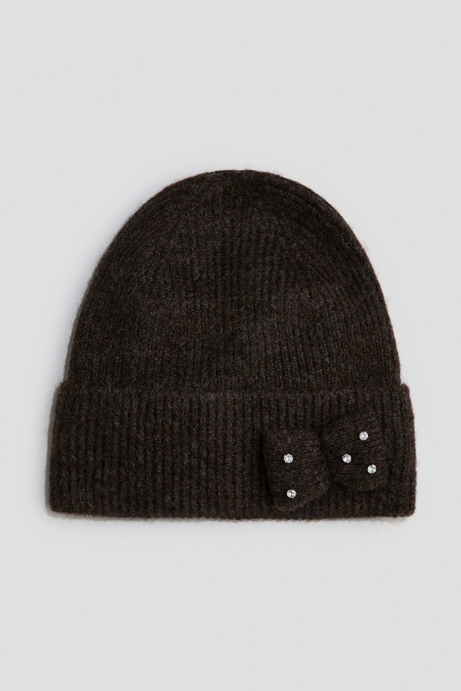 En mÃ¸rkebrun ribstrikket beanie er vist forfra og har en opfoldet kant. En matchende strikket slÃ¸jfe dekoreret med fem smÃ¥ rhinsten er fastgjort pÃ¥ hÃ¸jre side af kanten.