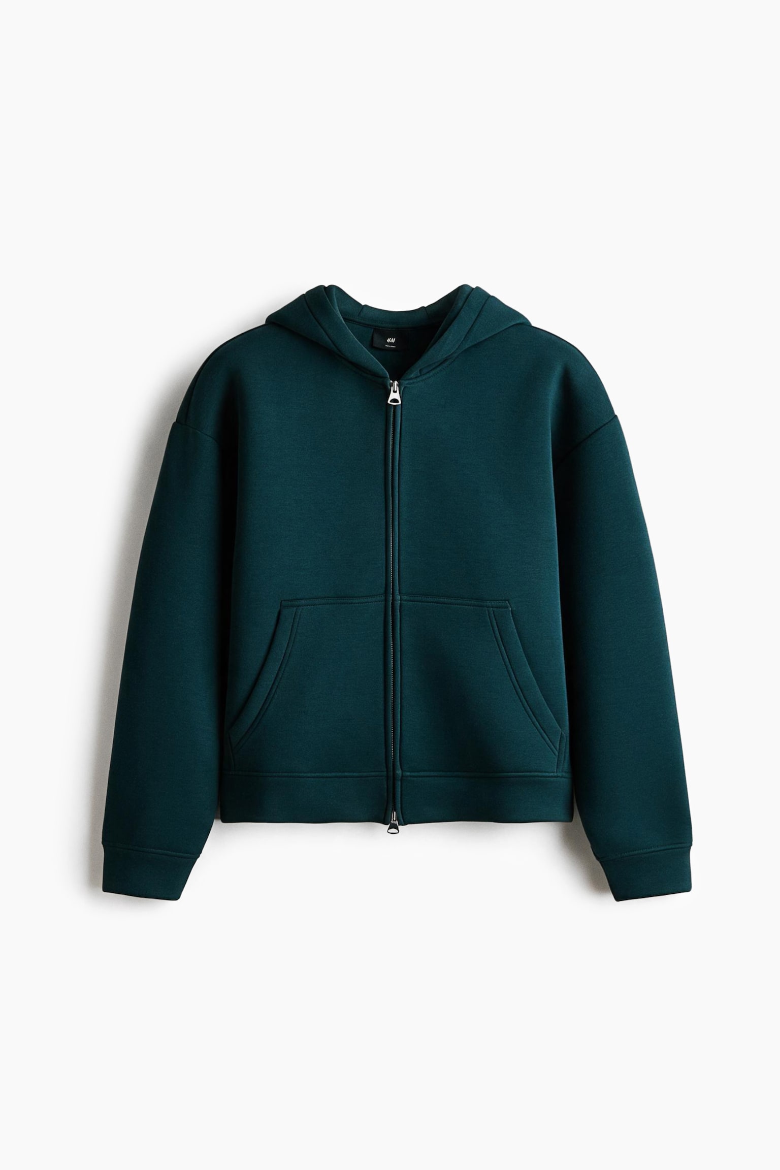 A dark teal, boxy-style zip-up hoodie in smooth scuba fabric is shown from the front, featuring a loose fit with dropped shoulders and a lined hood. The garment has a full-length front zip, open split-front pockets, and ribbed cuffs and hem.