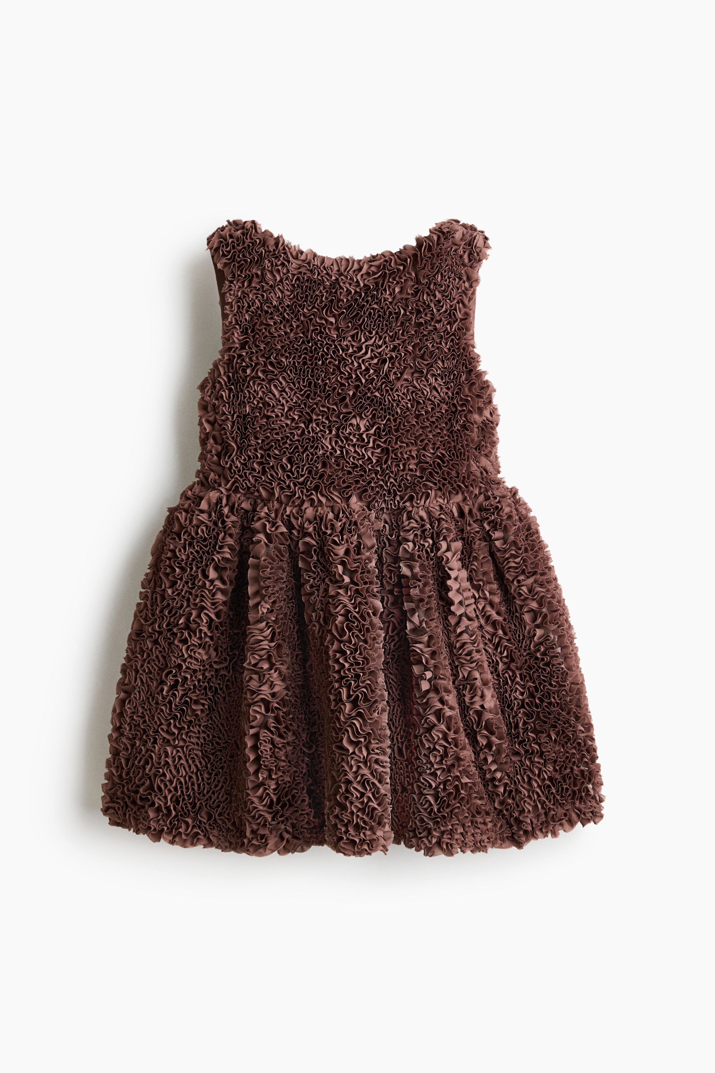 Une mini-robe sans manches marron texturÃ©e, ornÃ©e de dÃ©tails Ã  volants denses, est portÃ©e par le mannequin. La robe est associÃ©e Ã  un collant noir, et un petit sac Ã  main Ã  chaÃ®ne argentÃ©e est tenu derriÃ¨re le dos du mannequin.