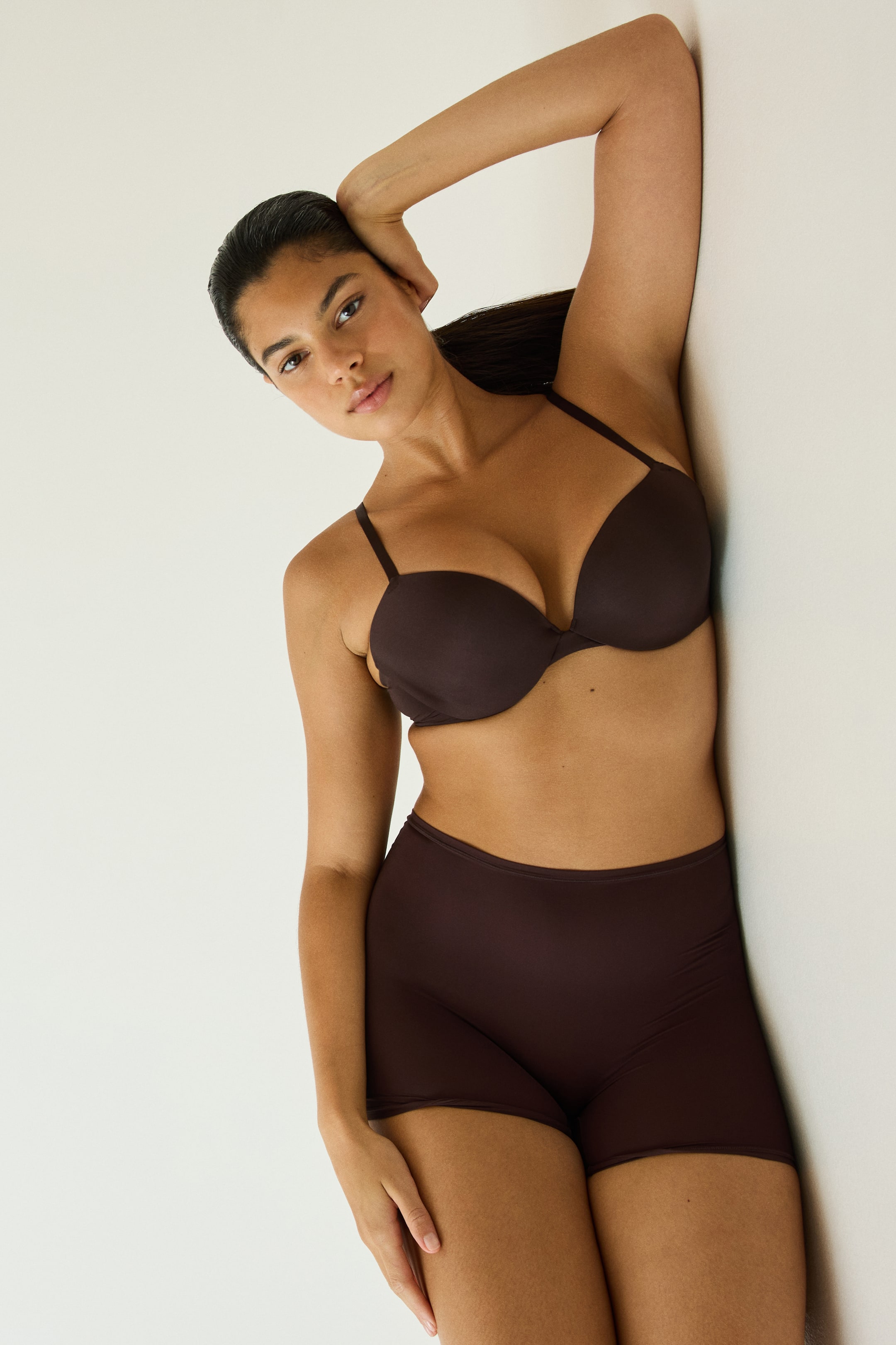 Büyük resmi görüntüle: Koyu kahverengi mikrofiber push-up sütyen; kalıplı, dolgulu ve balenli kupalara ile ince ayarlanabilir askılara sahip olup, model tarafından uyumlu yüksek bel şortla birlikte giyilmektedir.