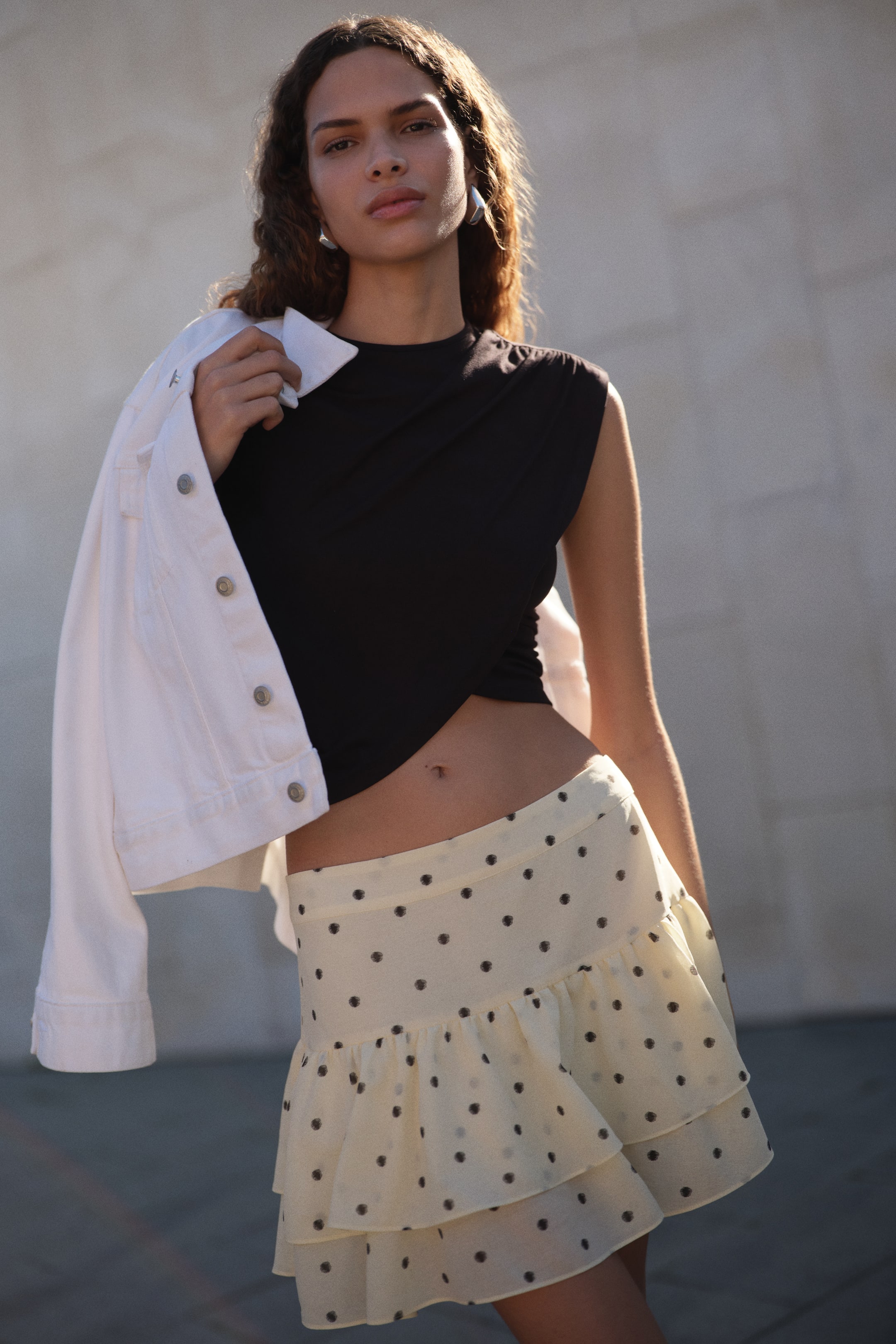 View larger image: A light yellow mini skirt showcasing a dark polka dot pattern, adorned with two tiered ruffles positioned at the waist, elegantly presenting its front-right side.