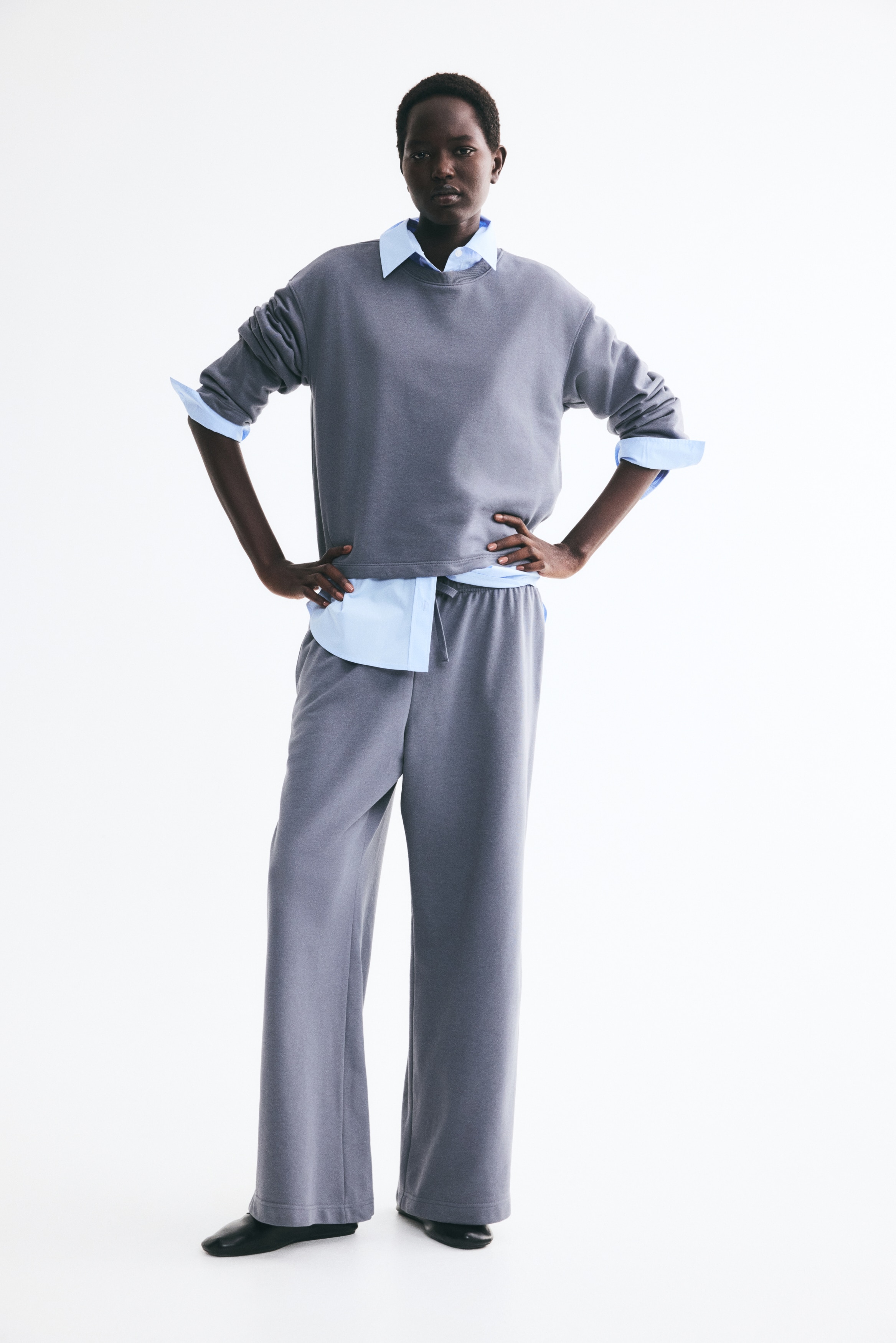 Ένα σετ loungewear δύο τεμαχίων σε ανθρακί γκρι χρώμα παρουσιάζεται από μπροστά. Το χαλαρό μακρυμάνικο τοπ διαθέτει στρογγυλή λαιμόκοψη και ίσιο στρίφωμα, που ακουμπά πάνω από το αντίστοιχο παντελόνι με φαρδιά μπατζάκια. Το παντελόνι διαθέτει ελαστική ζώνη μέσης και πλήρους μήκους, χαλαρή σιλουέτα.