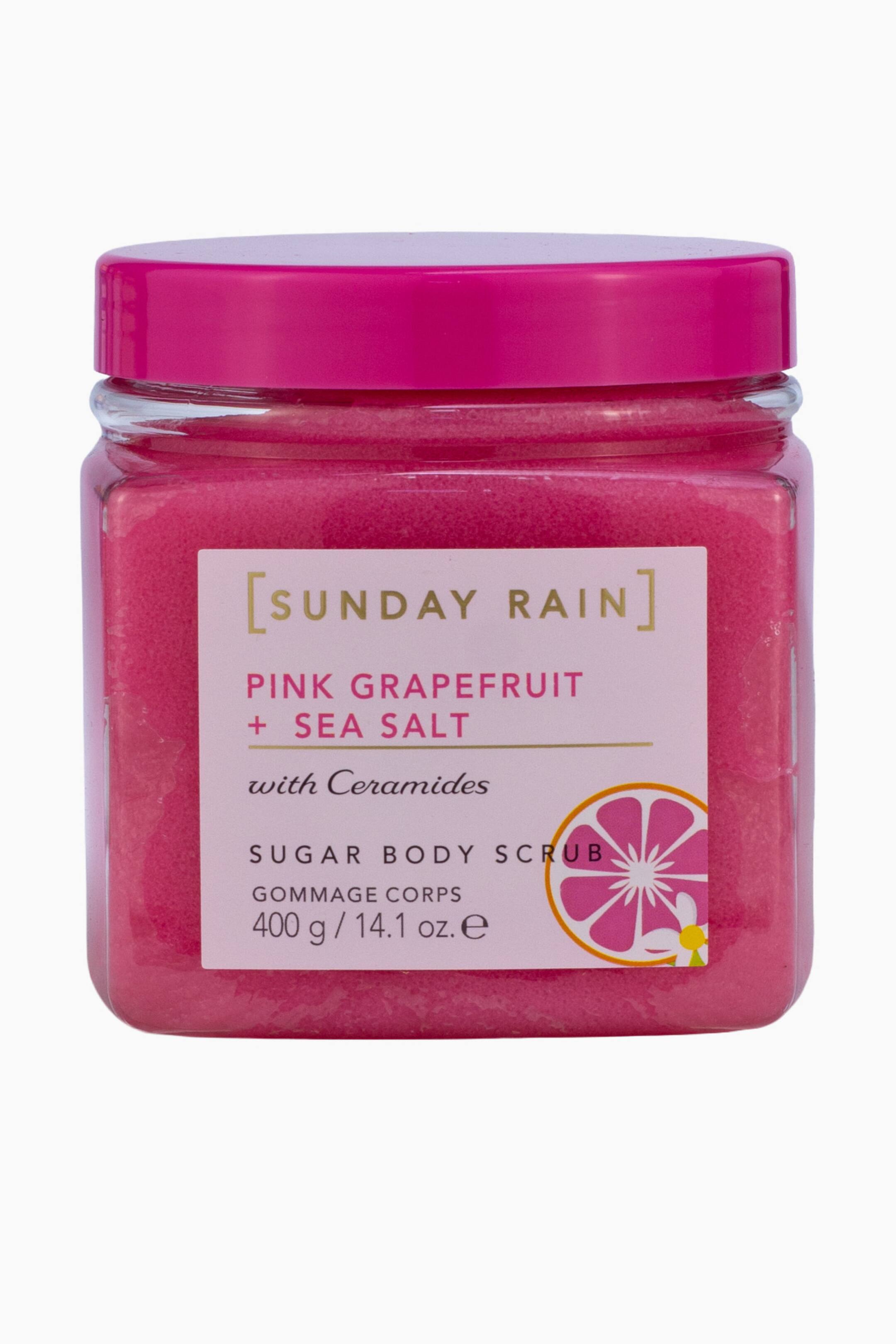 Visa större bild: En genomskinlig burk med en livfull rosa sockerkroppsskrubb är vänd framåt och har ett matchande rosa skruvlock. Den ljusrosa etiketten på framsidan visar varumärket "[SUNDAY RAIN]" och produktuppgifterna "PINK GRAPEFRUIT + SEA SALT with Ceramides" bredvid en grafisk illustration av rosa grapefrukt.