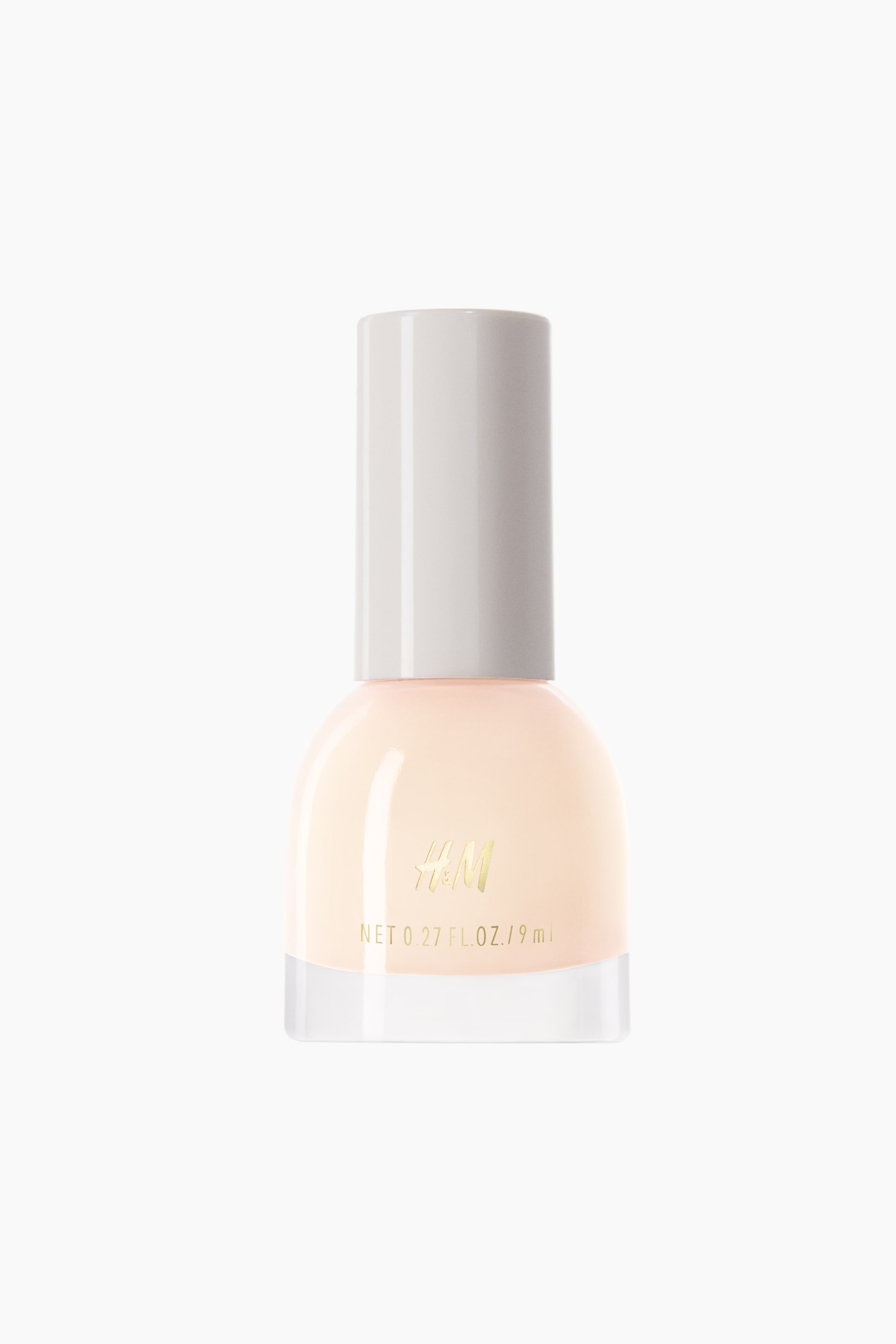 View larger image: A nail polish bottle showcases a translucent light peach polish inside its clear, rounded glass body, crowned with a light grey cylindrical cap. The gold "H&M" branding and "NET 0.27 FL. OZ. / 9 ml" text are prominently displayed on the front of the bottle.