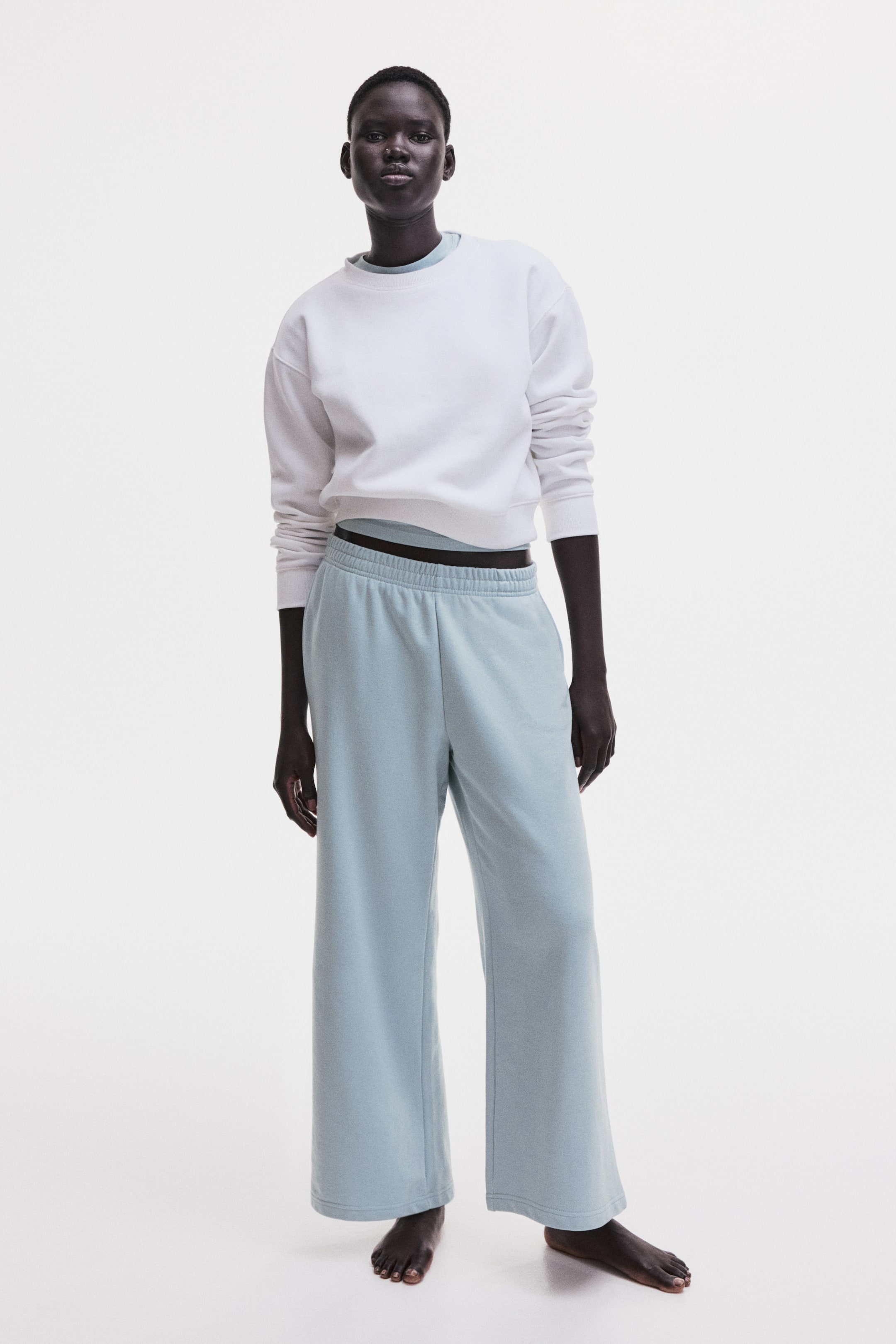 View larger image: A white long-sleeved crewneck sweatshirt, featuring ribbed cuffs and hem, is being worn over a light blue layer and paired with light blue wide-leg sweatpants. The sweatpants showcase an elasticated waistband and a relaxed, full-length fit, shown from a front-facing perspective.