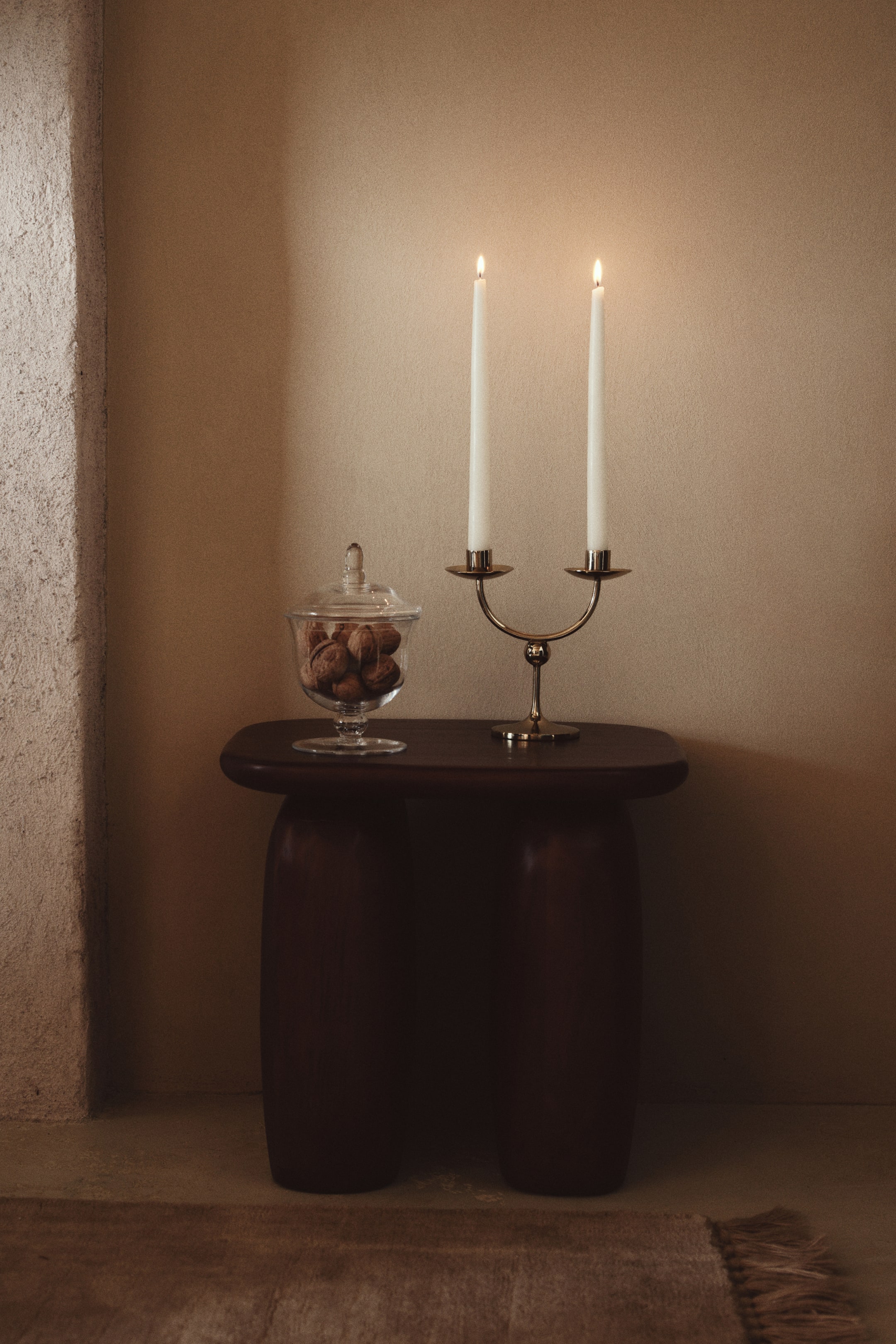 View larger image: A two-arm metal candelabrum is shown from the front, featuring a sleek U-shaped silhouette, a small spherical detail on the central stem, and a circular base. Two tall, lit white taper candles are resting in the candle holders.