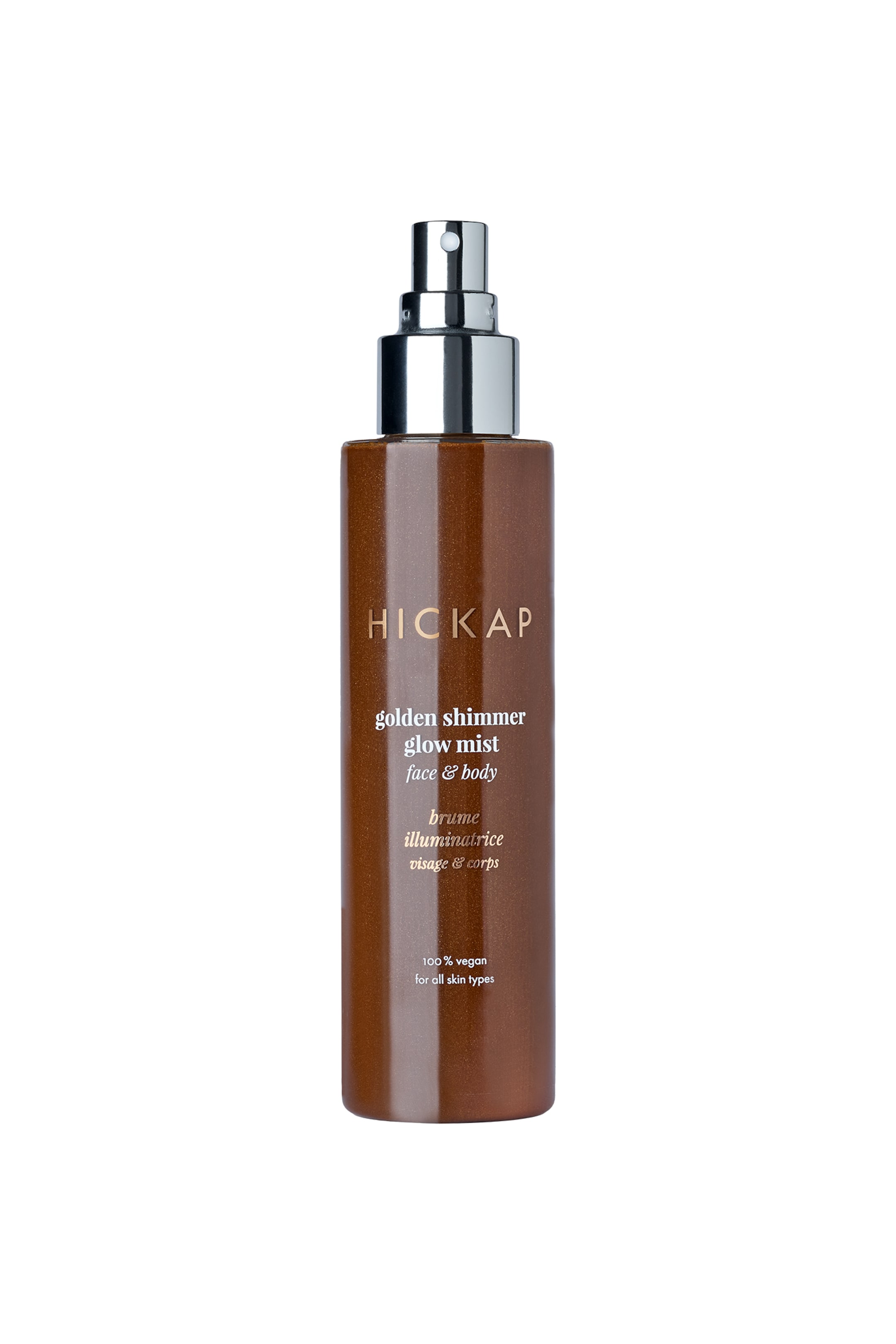 Vis større bilde: En sylindrisk, skimrende brun flaske med HICKAP golden shimmer glow mist står oppreist, vendt fremover. Den har en sølvfarget spraypumpe og hvit tekst på etiketten foran, som sier "HICKAP golden shimmer glow mist face & body" og "100% vegansk for alle hudtyper."