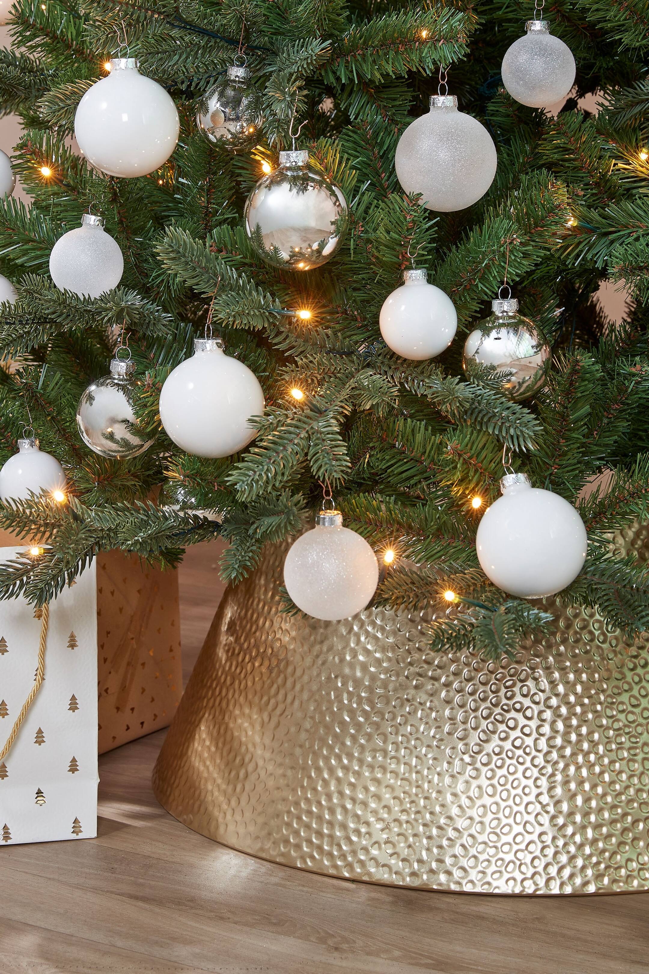 Grotere afbeelding bekijken: Een goudkleurige kerstboomrok toont zijn conische structuur, die naar de basis toe uitwaaiert. Het heeft een gehamerde, gedimpelde textuur over het gehele oppervlak.