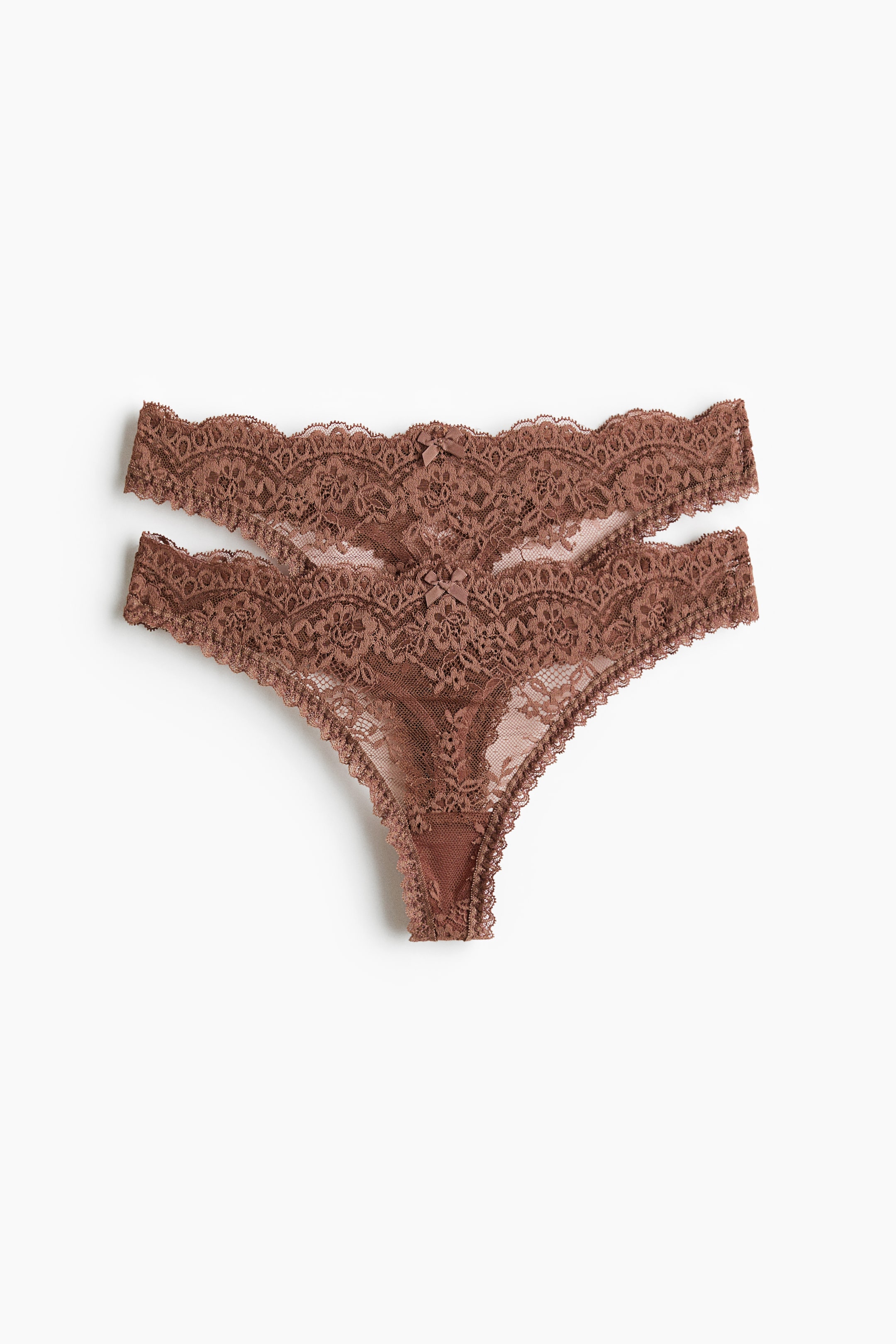 Grotere afbeelding bekijken: Twee bruine doorschijnende kanten string slips liggen plat en tonen een vooraanzicht met een lage taille, geschulpte randen en kleine decoratieve strikjes, met een gevoerd kruisje.