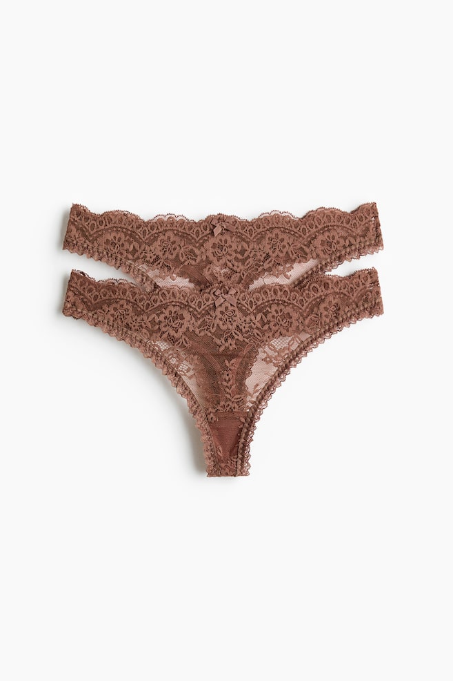 Zwei braune, transparente Spitzen-Tanga-Slips liegen flach und zeigen eine Vorderansicht mit niedrigem Bund, gewellten Kanten und kleinen Zierschleifen, die einen gefütterten Zwickel offenbaren. - 1