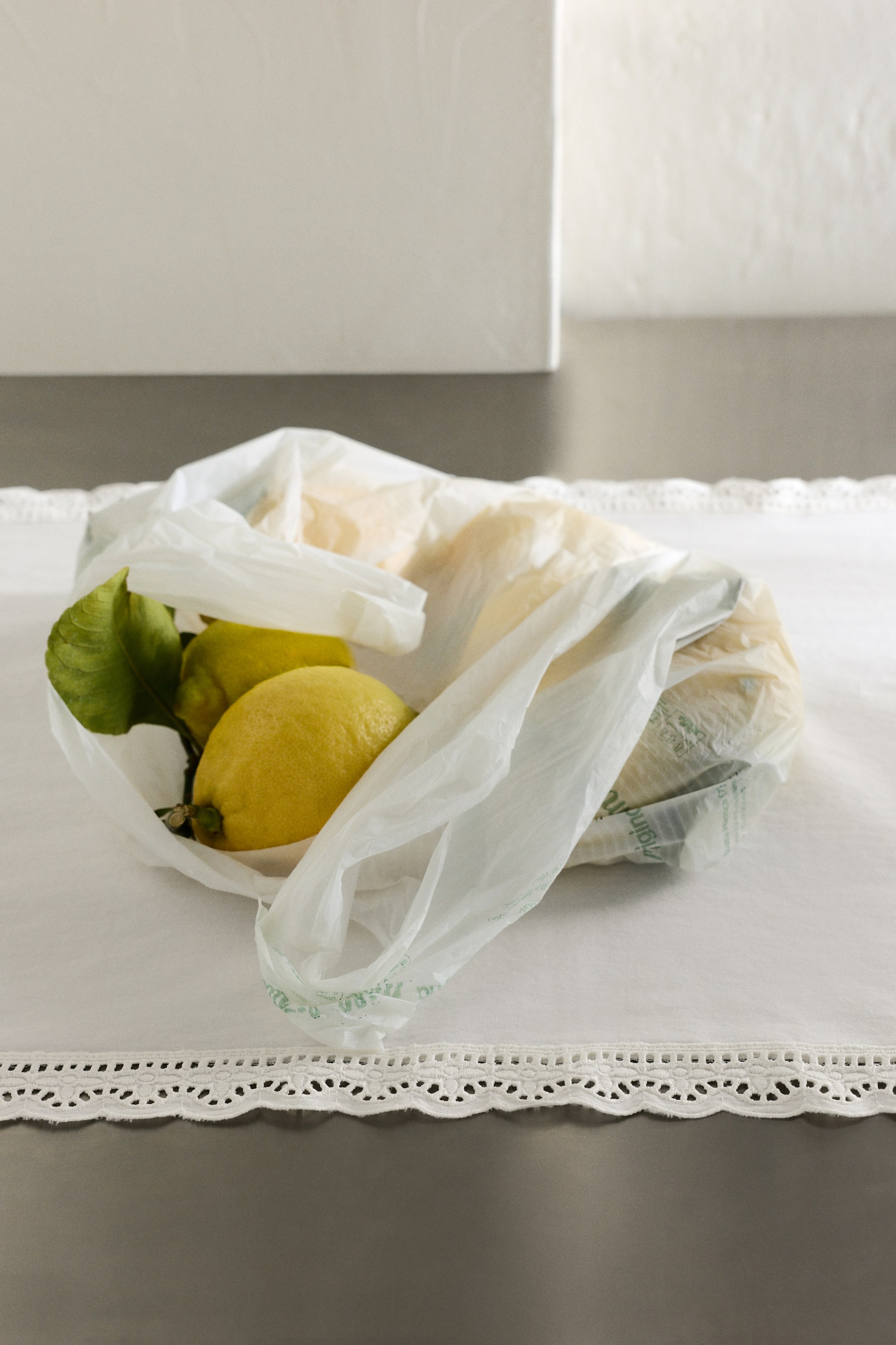 View larger image: Yellow lemons, some with green leaves, partially fill a translucent white plastic bag, which is presented at a slight angle.