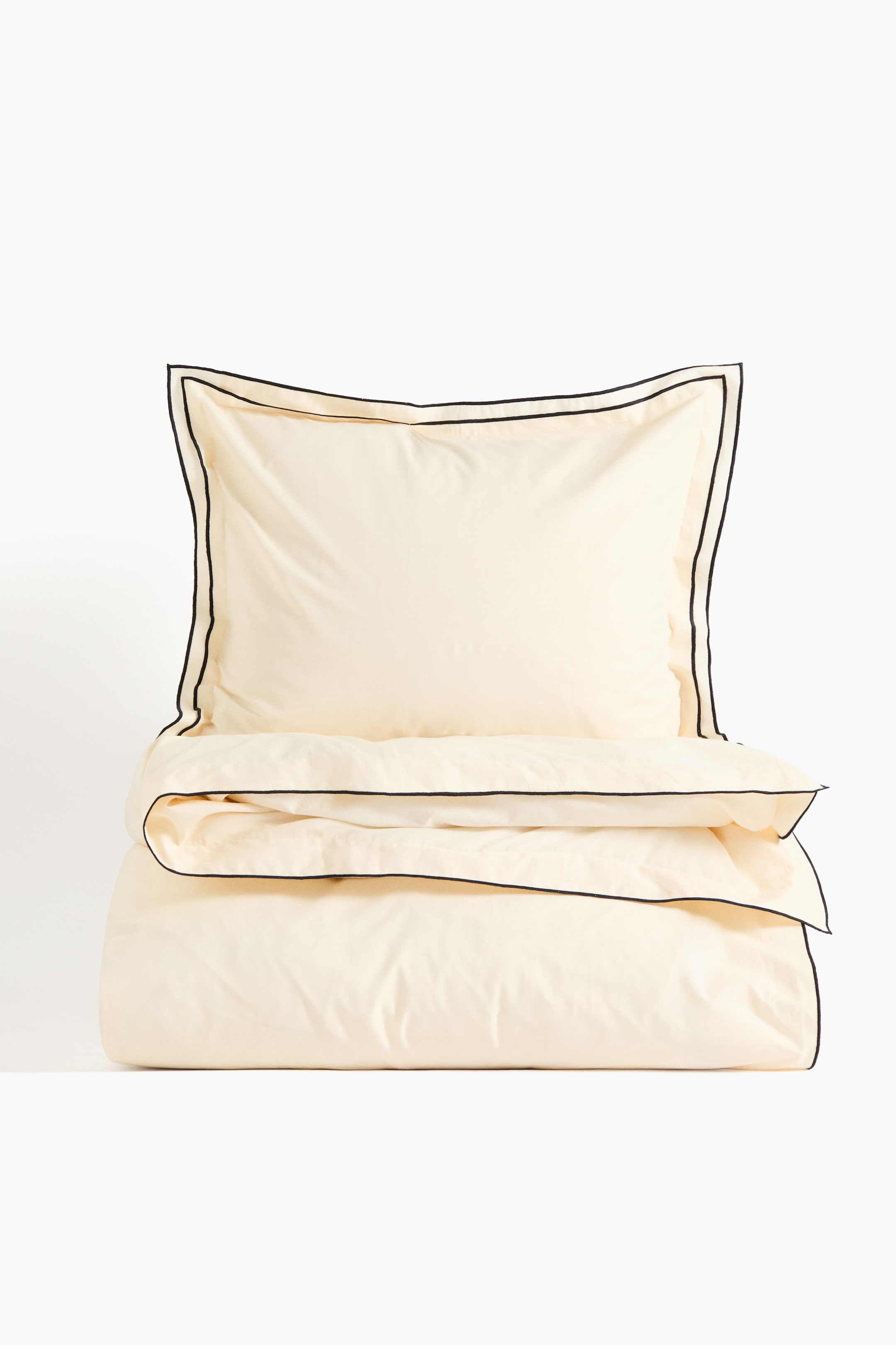 Ver imagen más grande: Un juego de funda nórdica individual color crema se muestra de frente. La funda de la almohada presenta un ribete de doble ala con dos líneas de adorno negro y descansa encima de la funda nórdica doblada, que muestra un ribete de ala simple con una línea de adorno negro a lo largo de su borde visible.