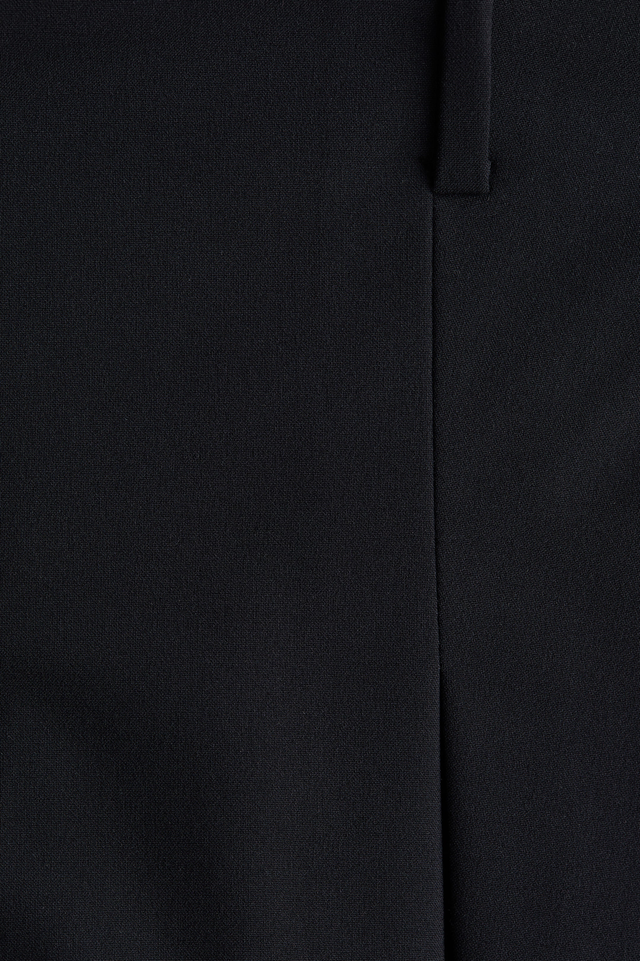 Ampliar la imagen: La mini falda pantalón negra está mostrando un primer plano de su tela tejida con textura sutil. Una costura vertical corre por el lado derecho de la prenda, y un lazo de tela horizontal aparece en la parte superior derecha.