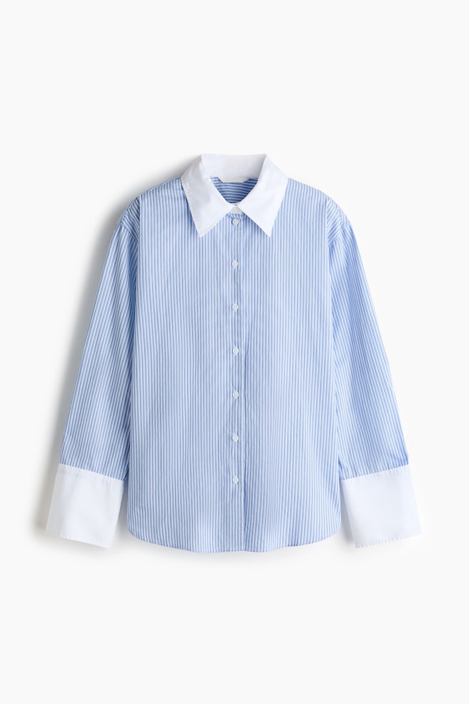 The oversized shirt is displaying a front view, featuring a blue and white vertical striped pattern with a fine ribbed texture, a contrasting white pointed collar, and a front placket with white buttons. It is showing dropped shoulders, long sleeves with wide, contrasting white buttoned cuffs, and a straight bottom hem. - 1