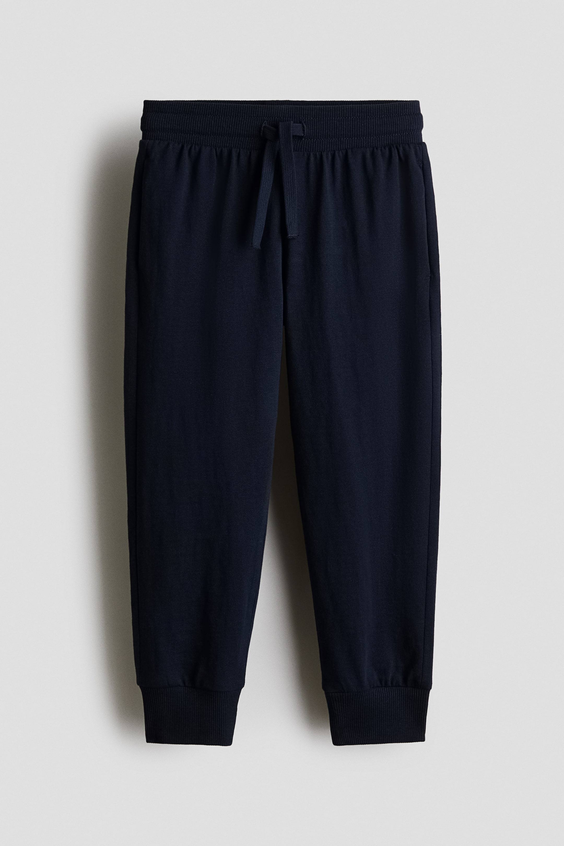 View larger image: Dark blue sweatpants are shown from the front, featuring an elasticated waistband with a tied drawstring, side pockets, and ribbed ankle cuffs.