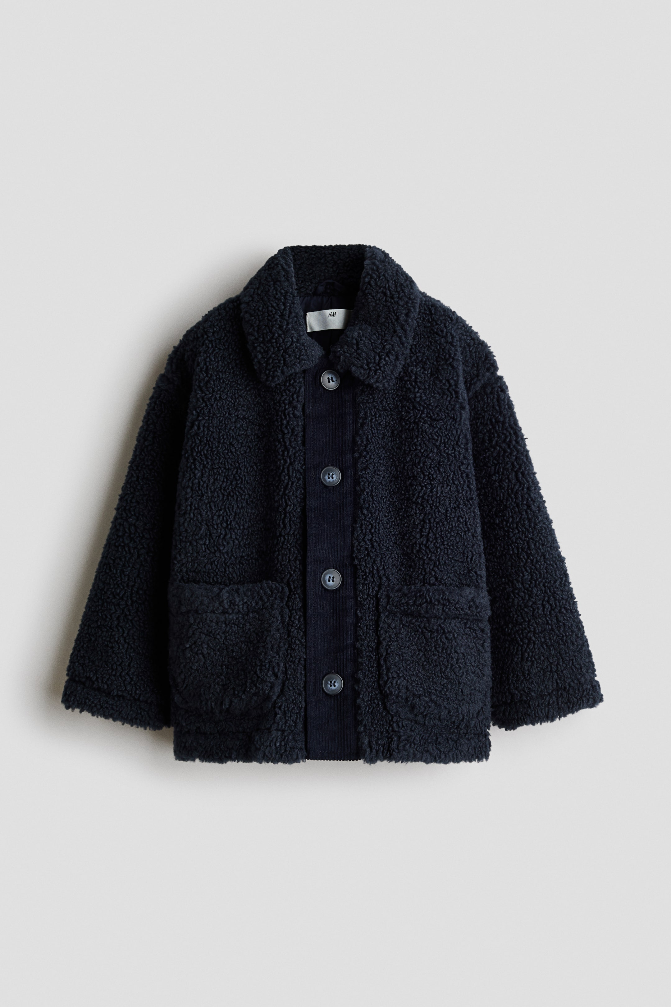 View larger image: A dark blue jacket is showcased at the front, featuring a textured teddy fleece material throughout its body and a spread collar. It highlights a corduroy button placket with five dark round buttons and two large patch pockets on the front.