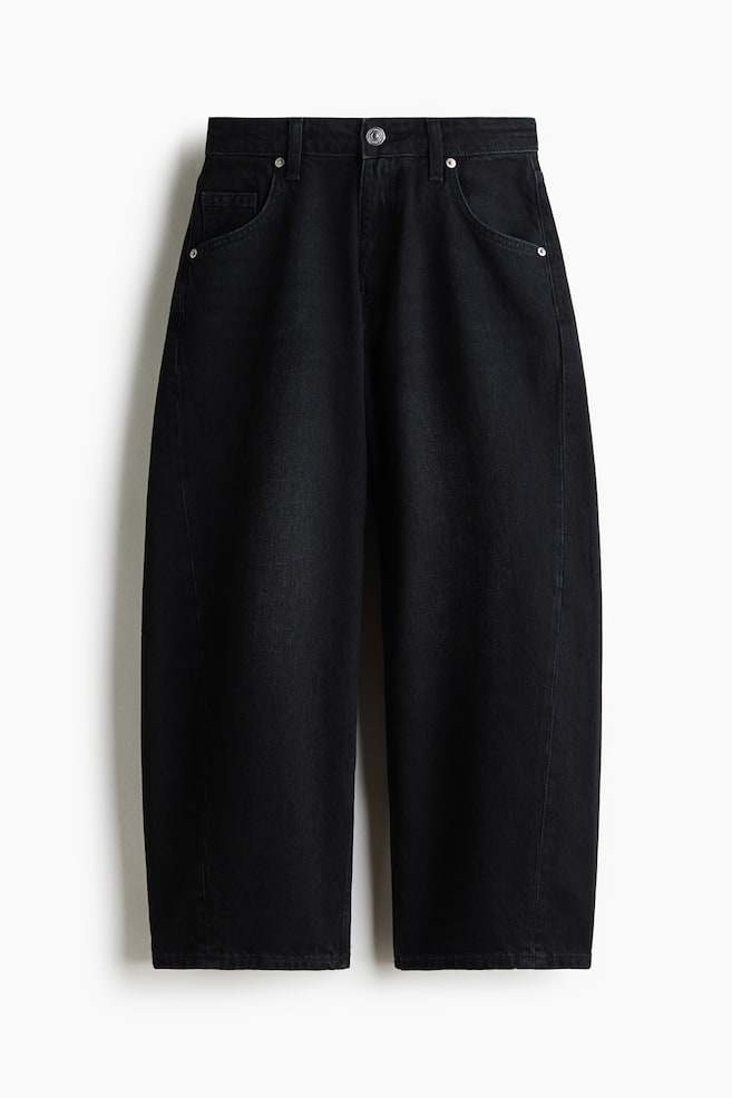 Jeans de ganga preta em algodão apresentados de frente, com cintura subida, fecho de correr e botão metálico. As pernas volumosas afunilam até uma bainha à altura do tornozelo, e são visíveis dois bolsos frontais curvos com rebites. - 1