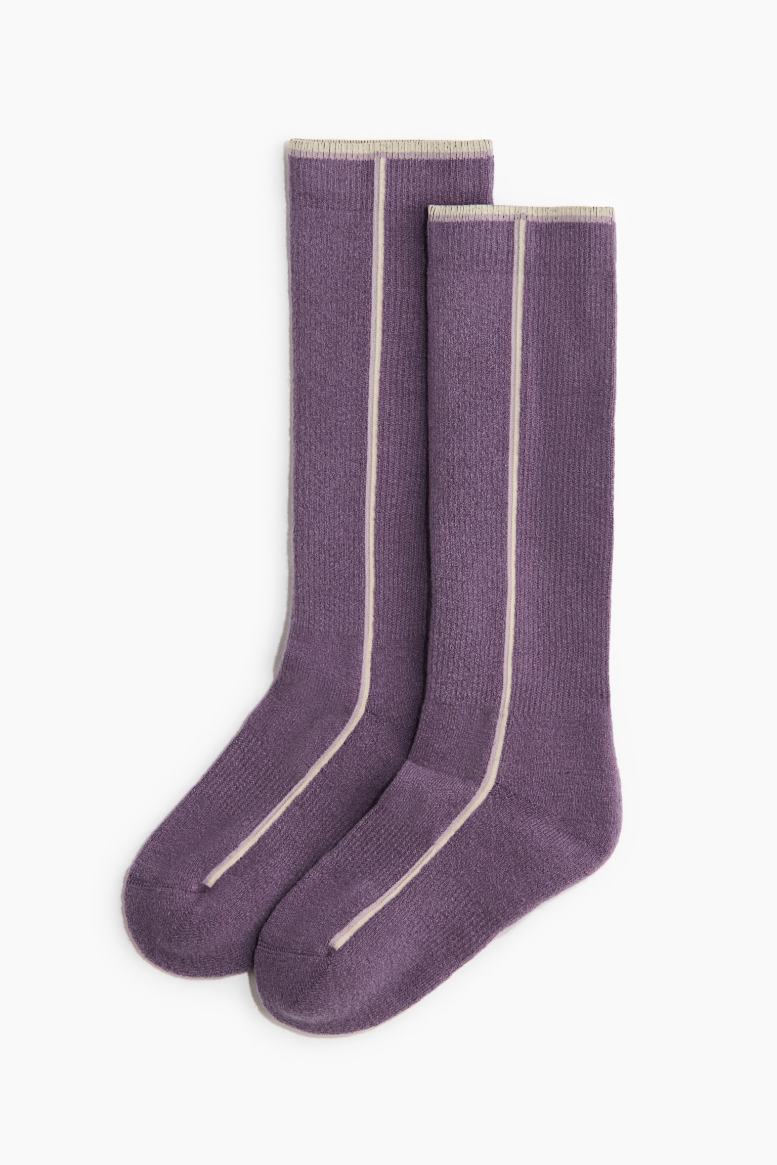 Ein Paar lila gerippte Stricksocken liegt flach und zeigt eine frontale Ansicht mit einem einzelnen vertikalen cremefarbenen Streifen, der mittig vom oberen Bund bis zur Spitze verlÃ¤uft. Die Socken haben eine passende cremefarbene Einfassung entlang der oberen gerippten BÃ¼ndchen.