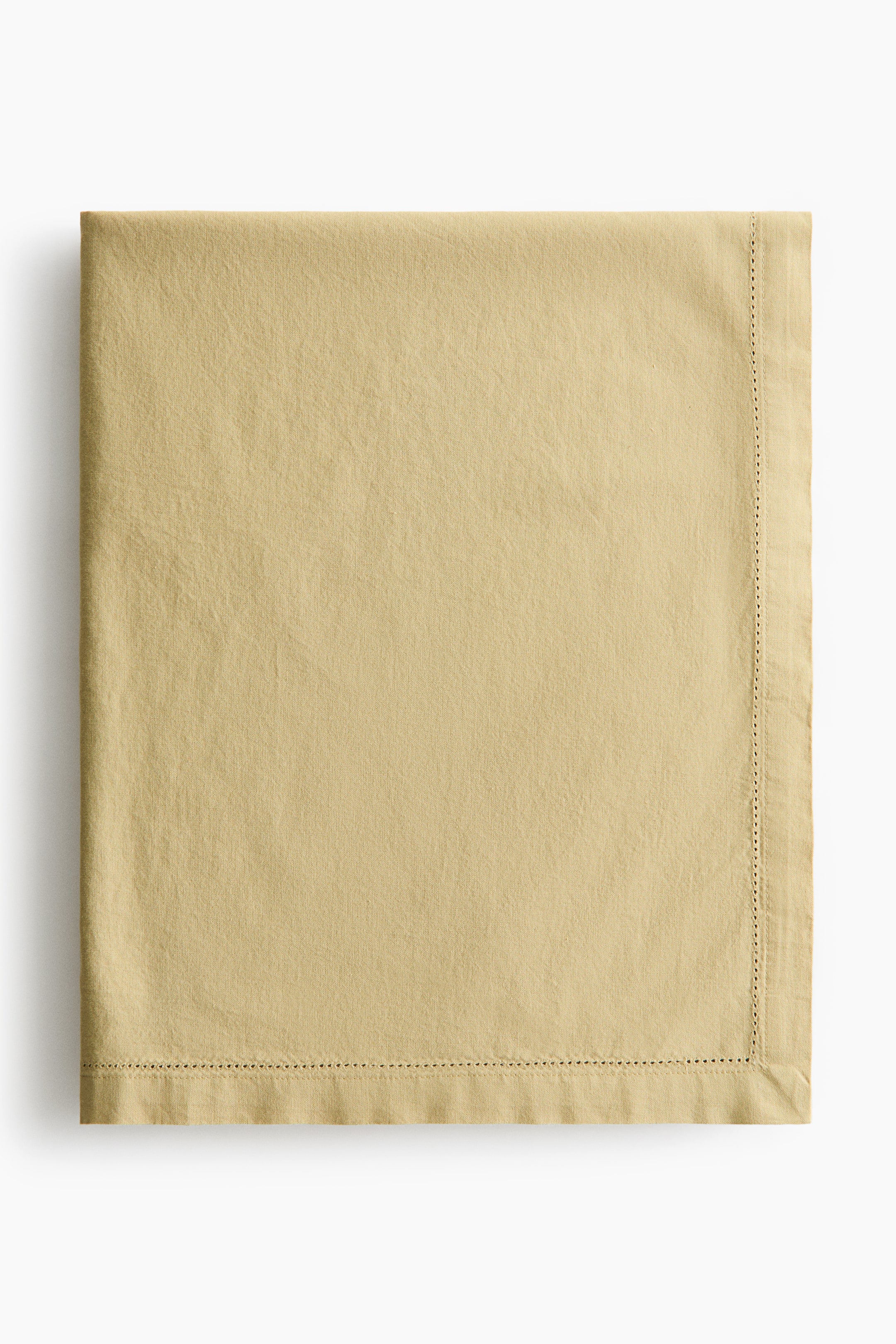 View larger image: A light beige cotton canvas tablecloth is displayed neatly folded, showcasing hemstitch detailing along its visible edges.