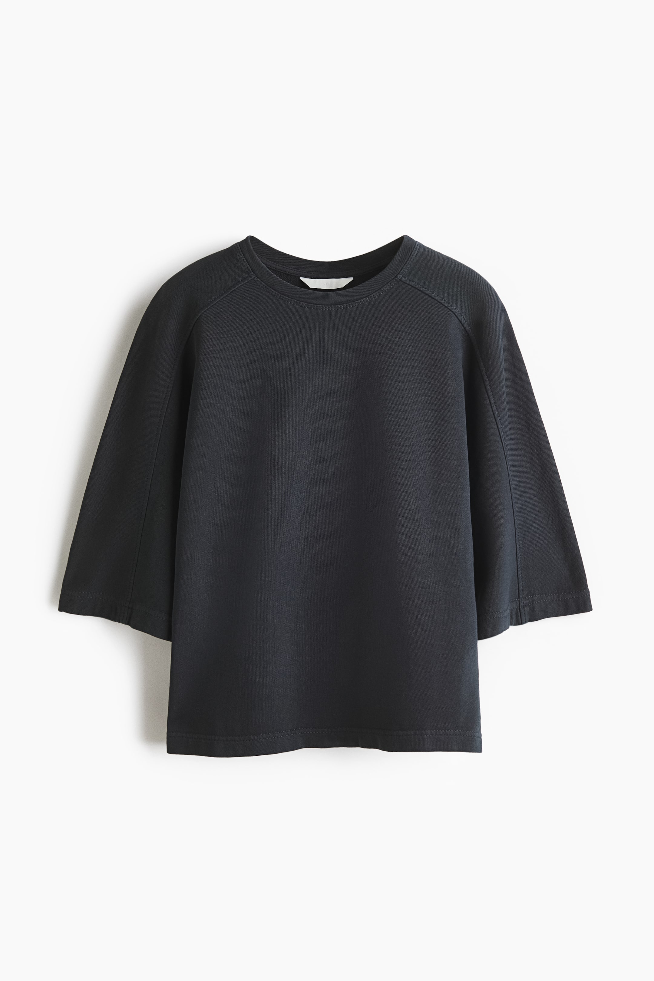 Agrandir l'image: Un haut gris foncé à coupe ample est orienté vers l'avant, révélant un col rond et des manches raglan larges de longueur 3/4 avec des coutures apparentes. Il présente un ourlet droit et un tissu de sweat en coton lisse et léger.