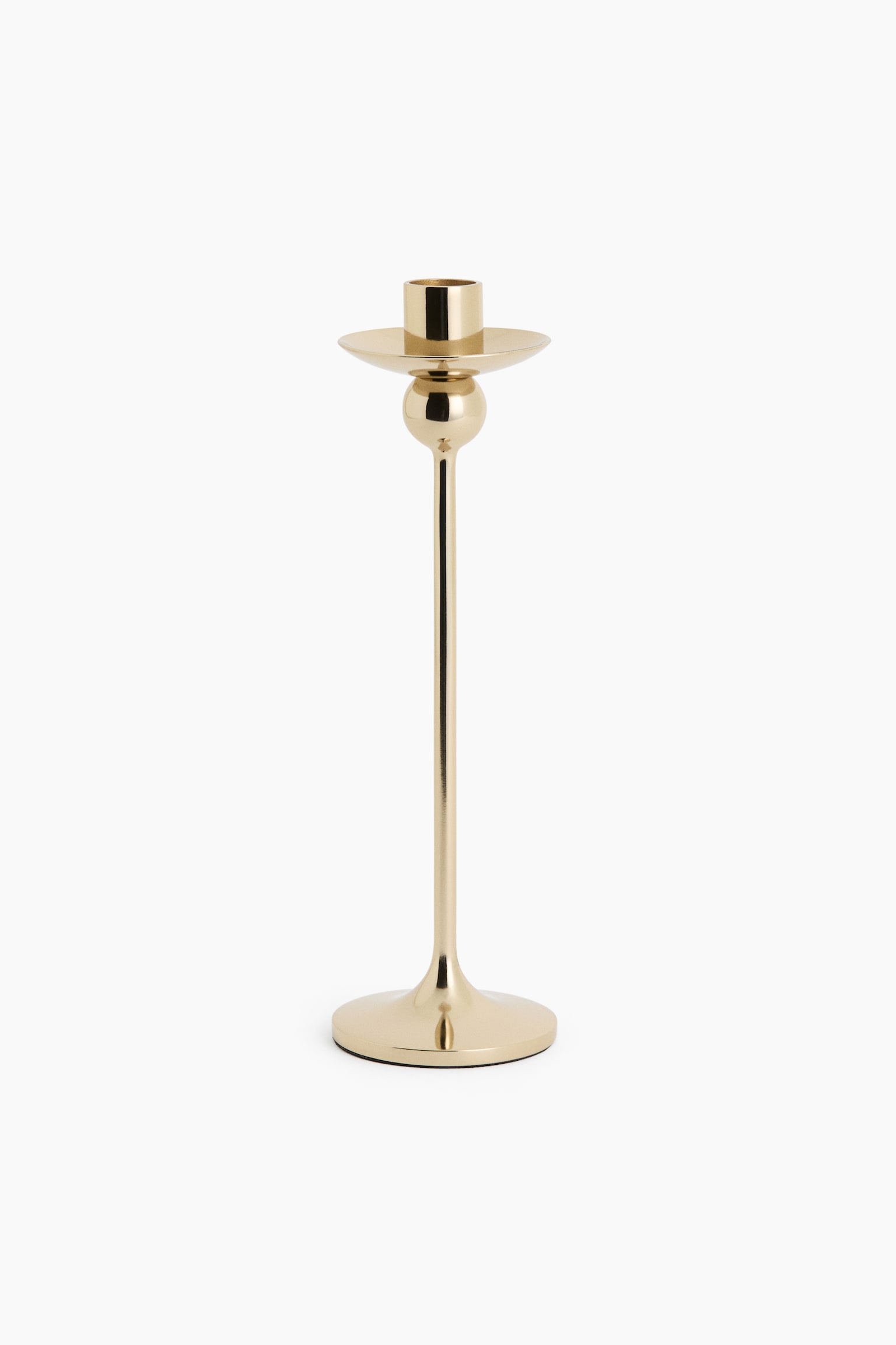 A polished gold-finished stainless steel candlestick stands upright, featuring a sleek, slender stem rising from a flared circular base. The design showcases a spherical detail positioned directly beneath a shallow drip pan and a cylindrical candle holder at the top.