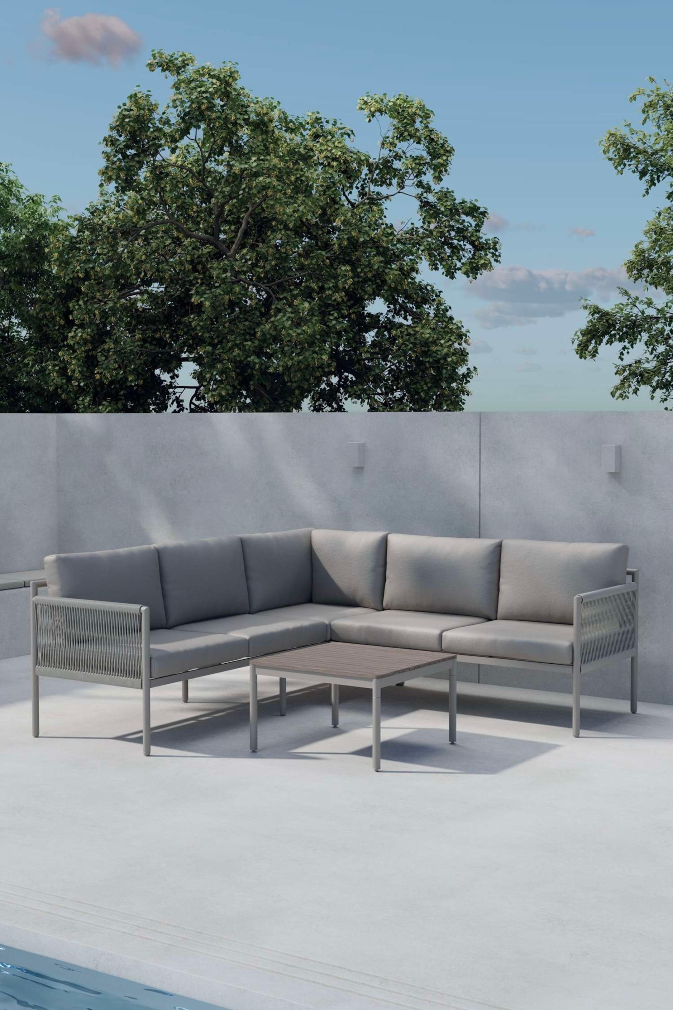 Agrandir l'image: Un canapé d'angle extérieur en forme de L présente une structure en métal gris clair avec des accoudoirs et dossiers en corde tressée, ainsi que des coussins gris clair. Une table basse rectangulaire assortie est placée devant le canapé, arborant un plateau à lattes.