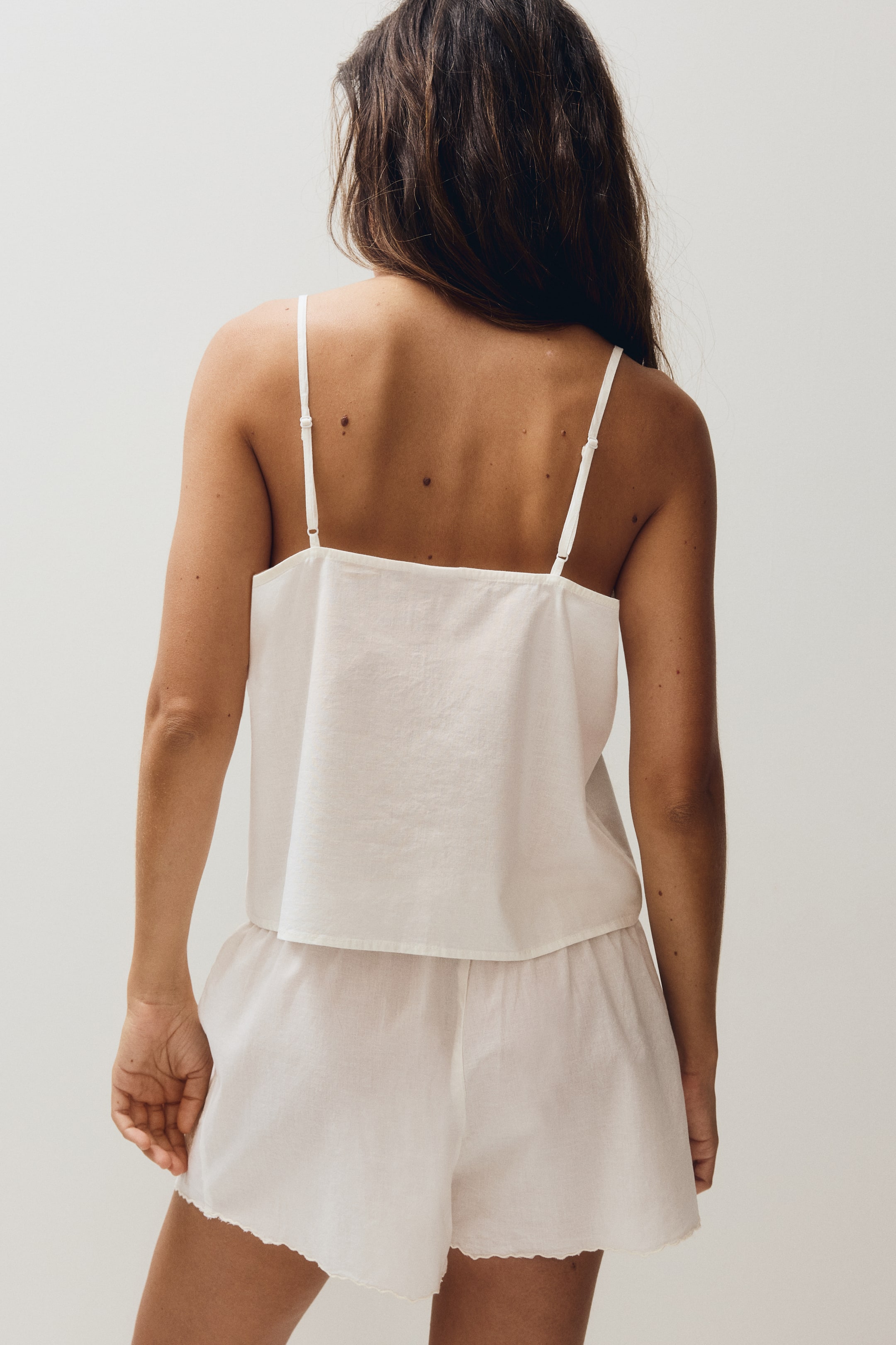 Ver imagen más grande: Un conjunto de dos piezas en color blanco, que incluye un top camisola y unos pantalones cortos, se muestra desde atrás. La camisola presenta finos tirantes ajustables tipo espagueti y una silueta relajada, mientras que los pantalones cortos exhiben un dobladillo festoneado.